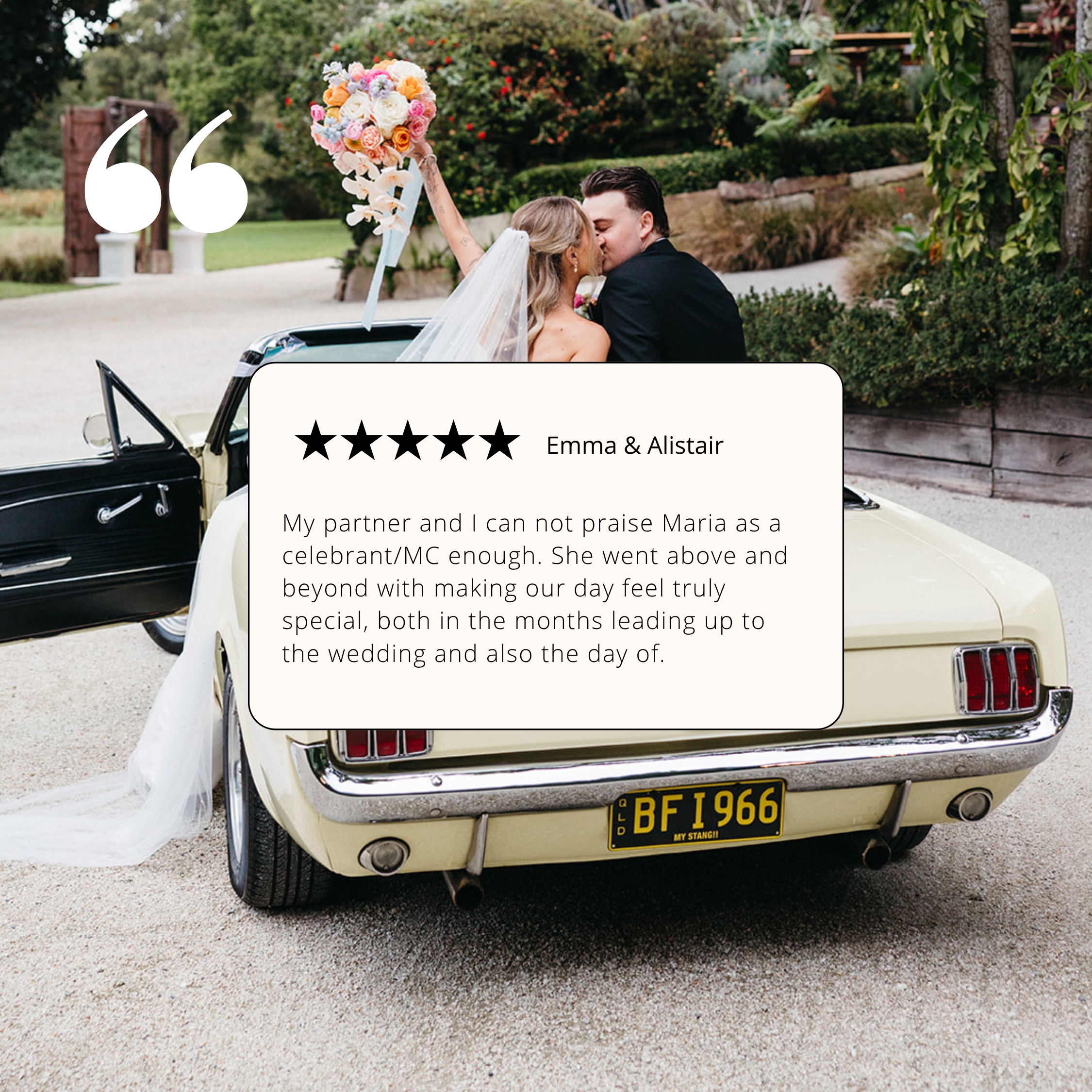A vintage white convertible car with a floral wedding decoration on the hood, parked outdoors on a gravel surface, with a background of green trees and shrubs.