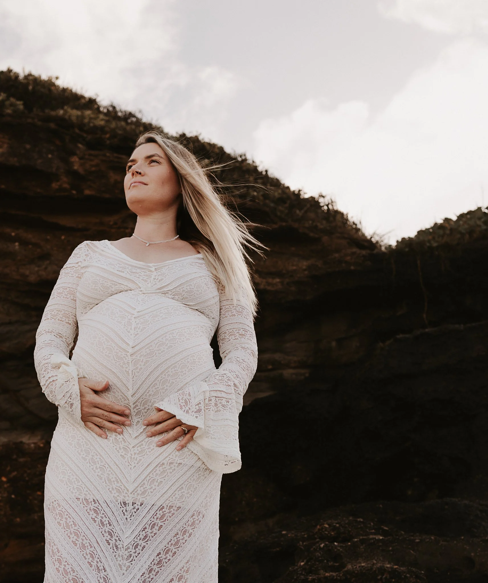 Pregnant mother cradling bump in white dress at Caves Beach NSW