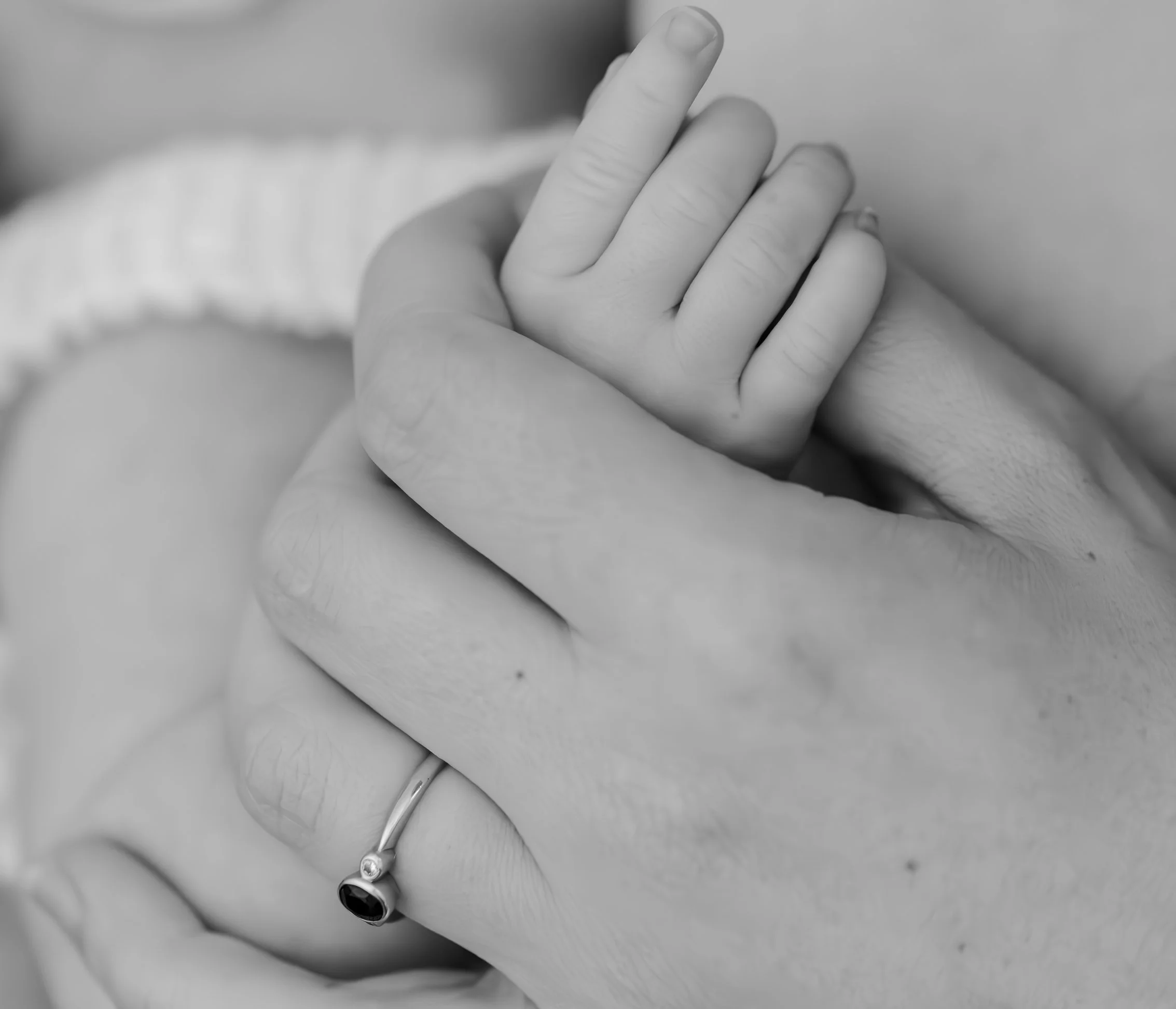 Close-up of a baby's hand grasping an adult's finger, both hands showing a gentle grip, in black and white during Newborn session in Lake Macquarie