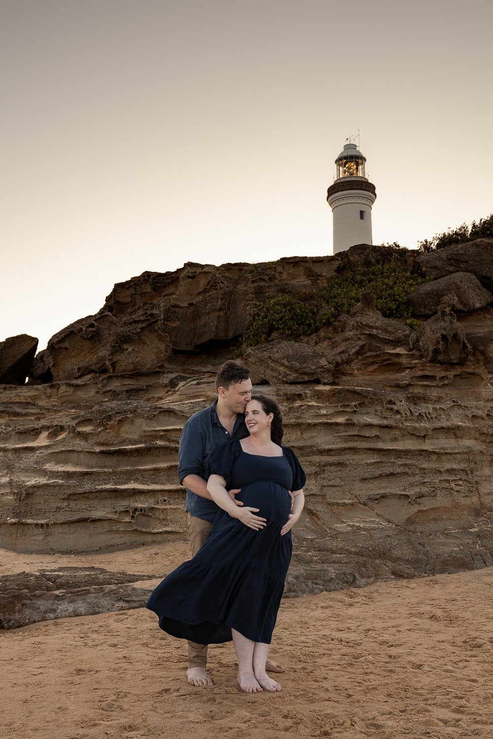 Nicole Johnson Photography ~ Maternity Beach session, embracing in front of cliff face and lighthouse