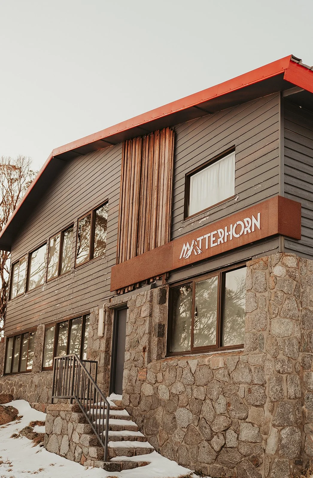 A two-story building with stone and wood exterior, multiple windows, and a sign that reads 'Matterhorn.' There is snow on the ground and steps leading up to the entrance.