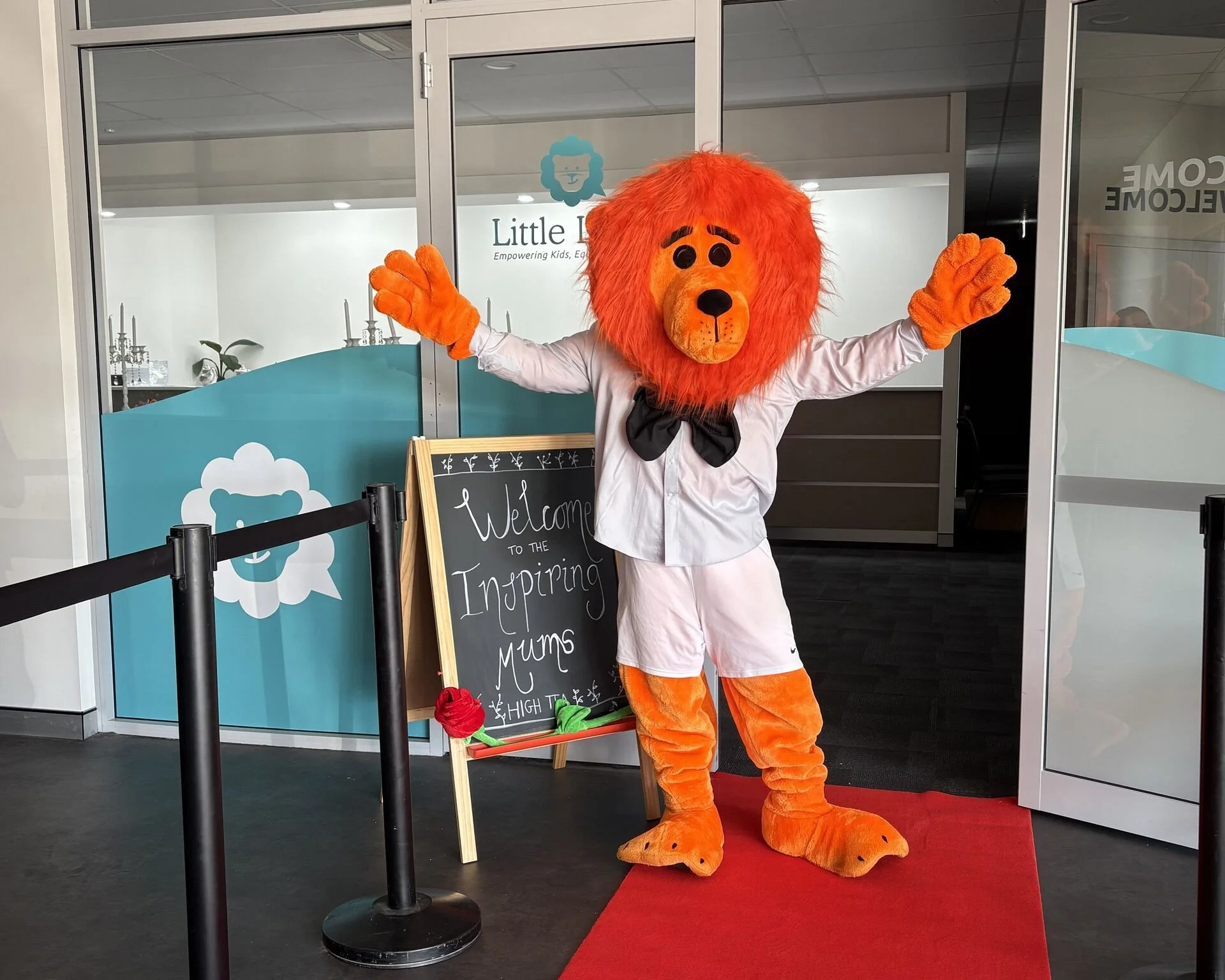 Little Lions mascot wearing a bow tie welcoming guests to the Inspiring Mums High Tea event at the clinic entrance