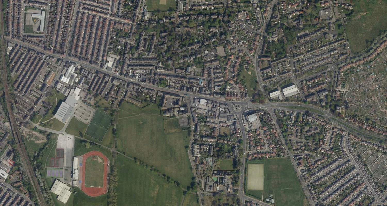 An aerial view of a neighborhood featuring residential streets, a park with a sports field and running track, and a complex of sports facilities, including tennis courts.