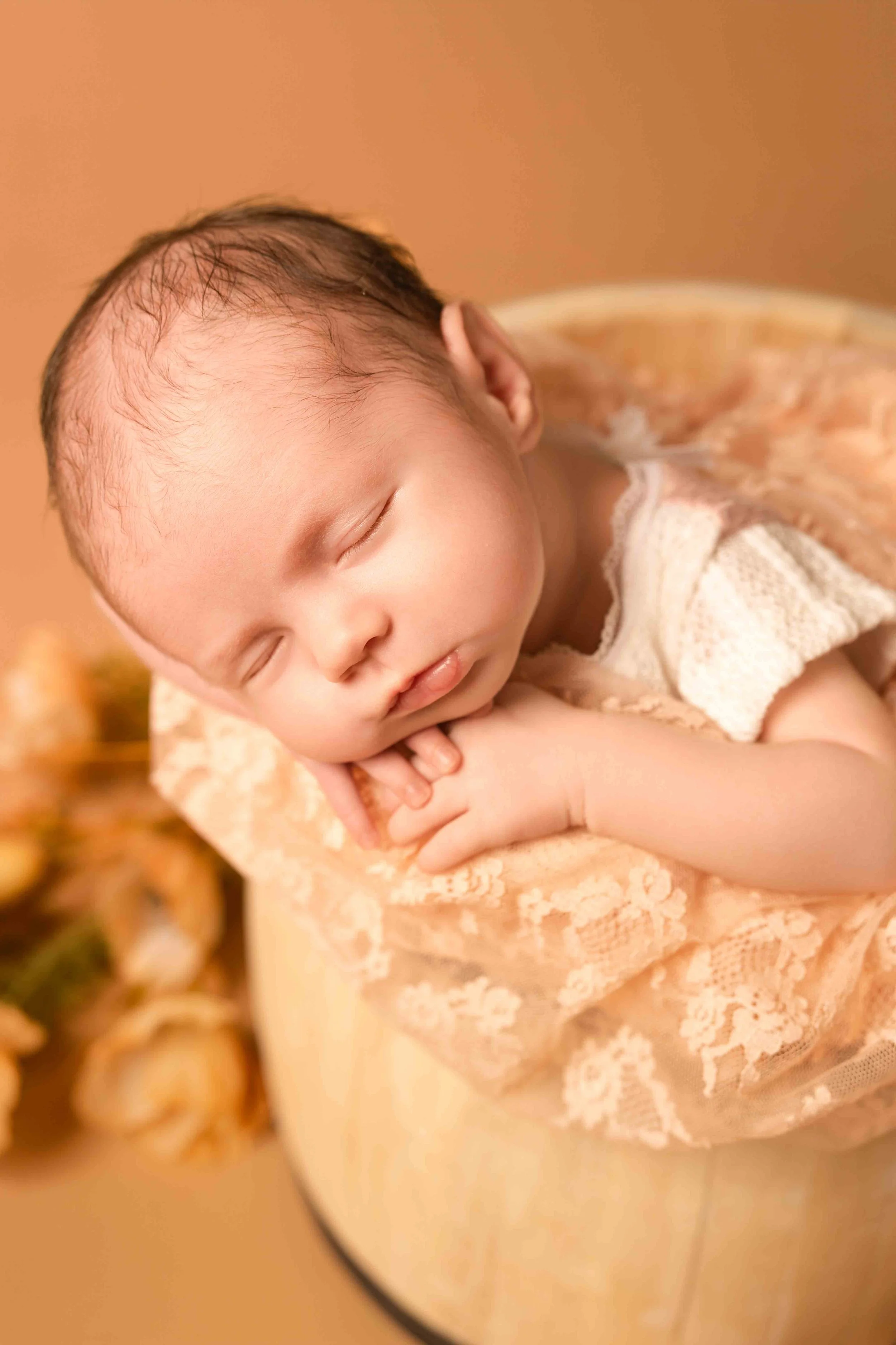 Ein kleines Baby schläft mit geschlossenen Augen, eingekuschelt in ein lila und weiße Kleidungsstück, auf einem weichen Kissen.