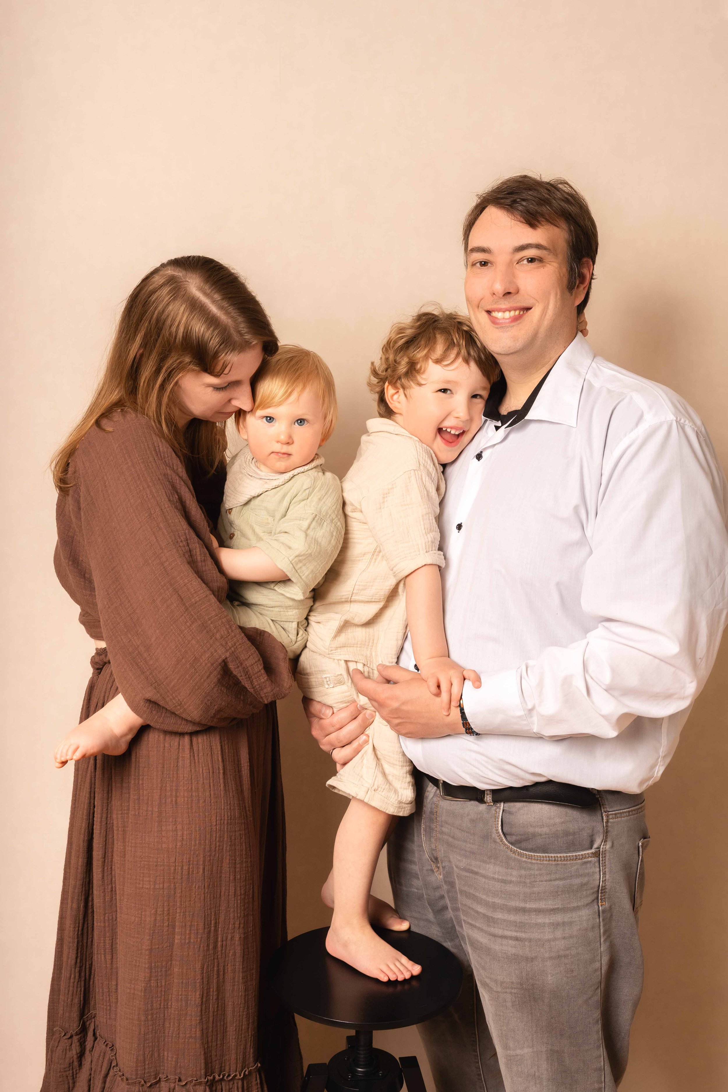 Eine glückliche Familie mit zwei kleinen Kindern vor einem neutralen Hintergrund.