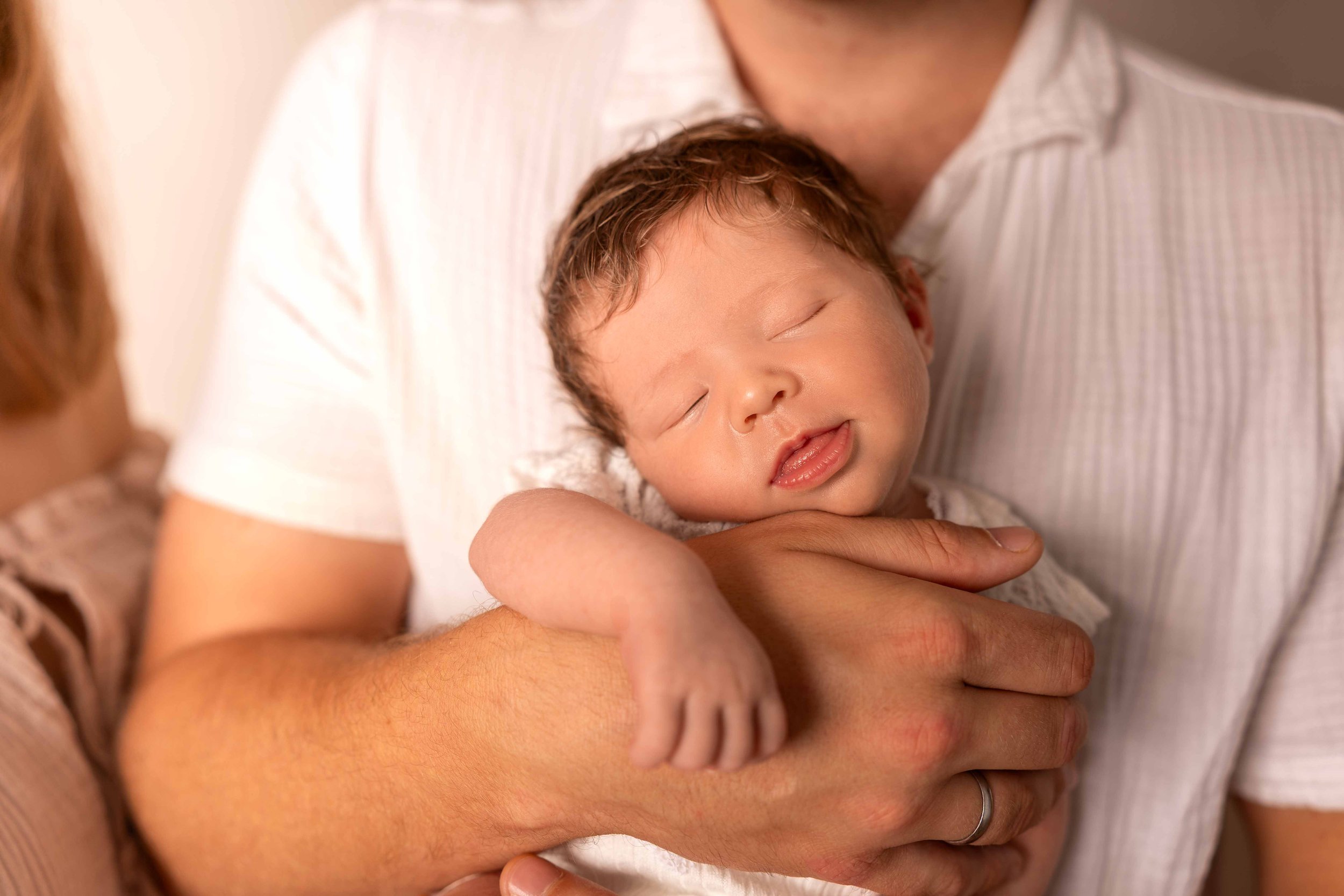 Ein Baby wird sanft von einem Erwachsenen gehalten, die Augen sind geschlossen und es sieht friedlich aus.