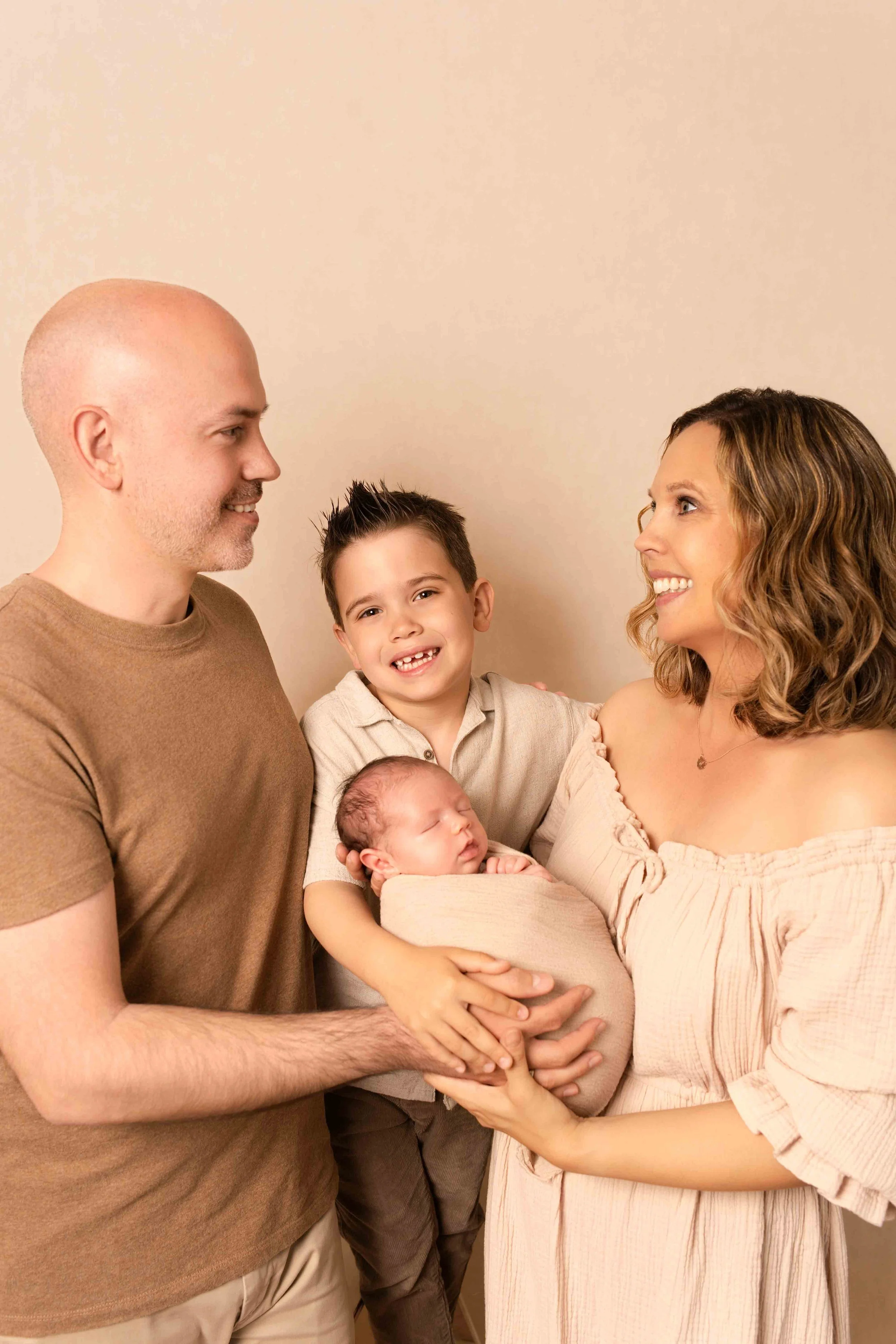 Familie mit Vater, Mutter, zwei Kindern und einem Neugeborenen, die sich liebevoll um das Baby versammeln.