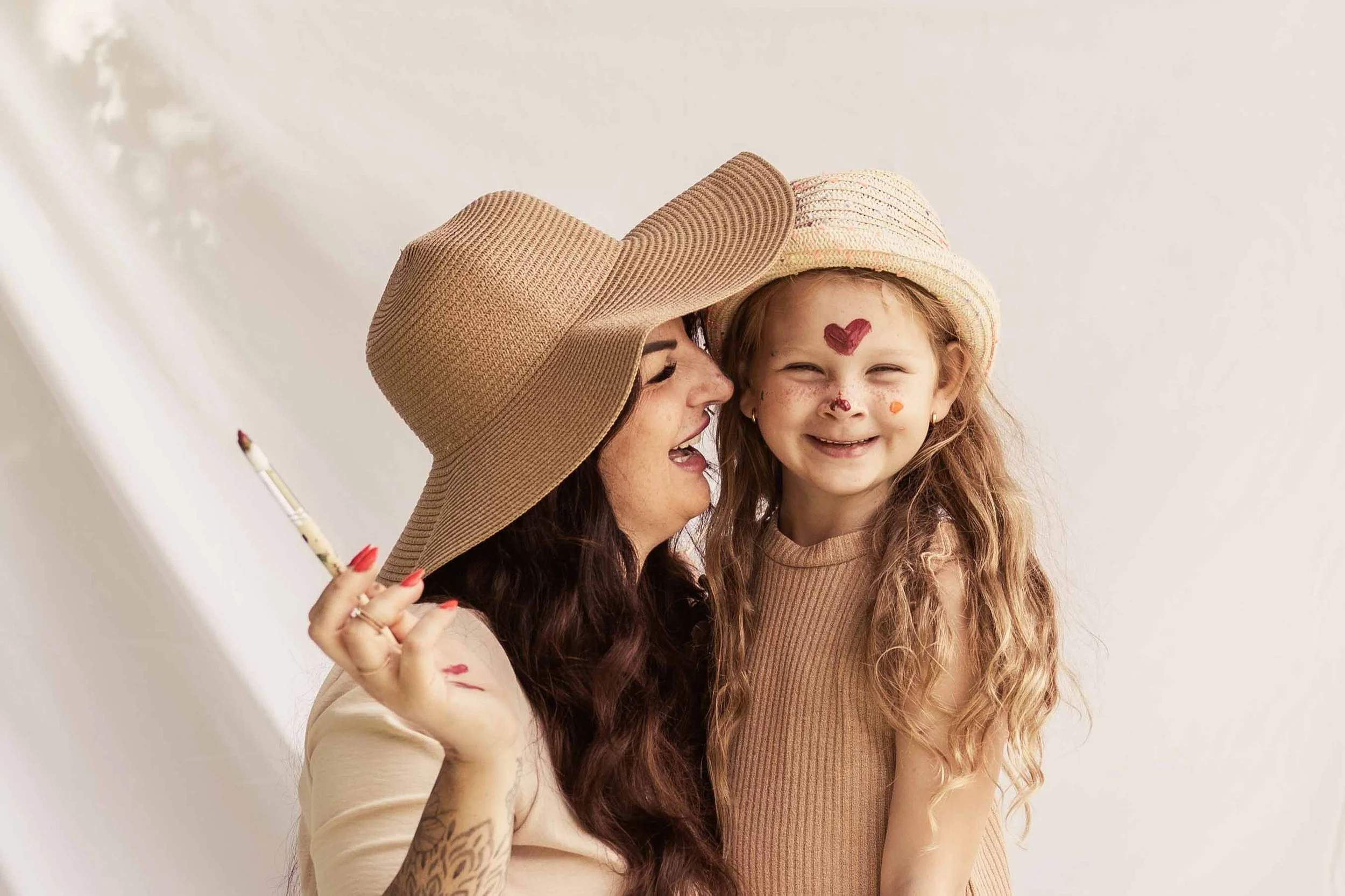 Eine Frau und ein Mädchen fühlen sich lieben und lachen glücklich, mit Sonnenhüte, das Mädchen hat Gesichtsbierbemalung