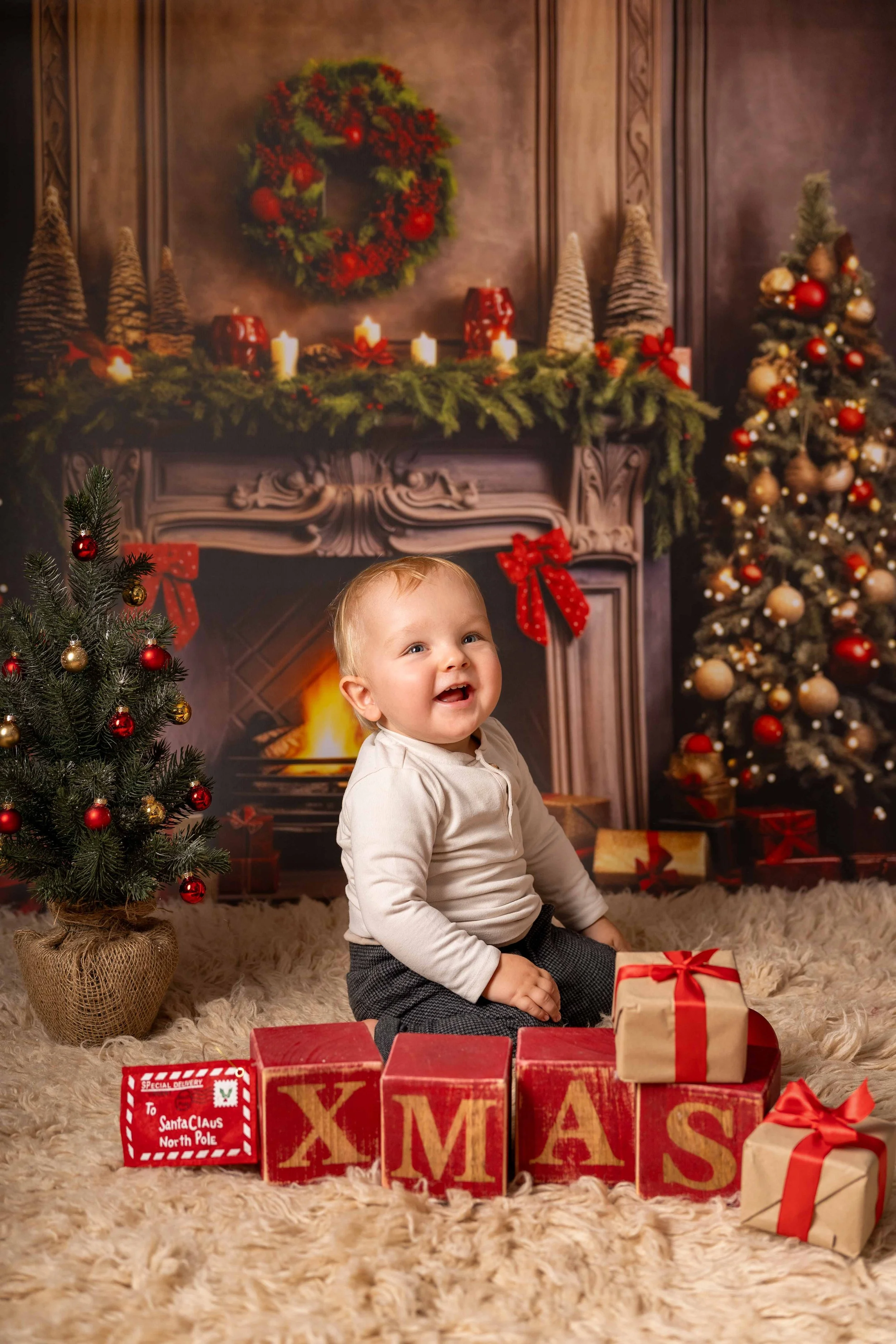 Ein Kinderjunge sitzt auf einem flauschigen Teppich vor einer weihnachtlich dekorierten Kulisse mit einem Kamin, Tannenbäumen und Geschenken, umgeben von Weihnachtsdekoration.