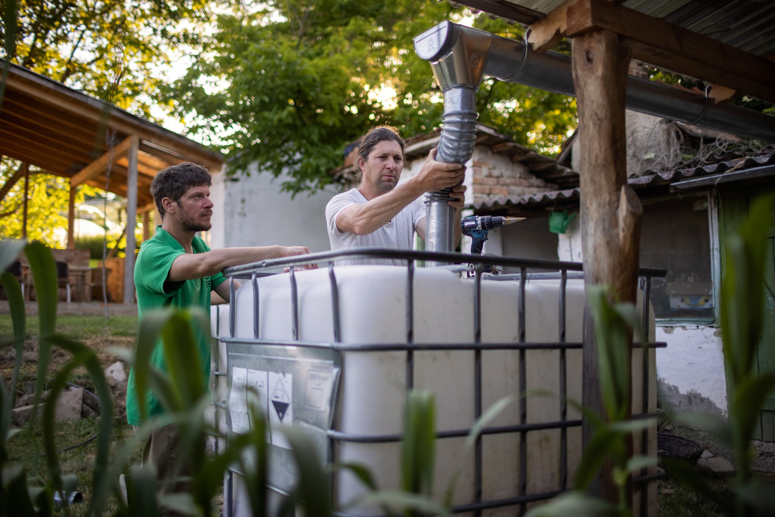  To catch and utilize rainwater, Gergő and Dani install water collection tanks at the community center in the village. Nyim, May 22, 2022. 