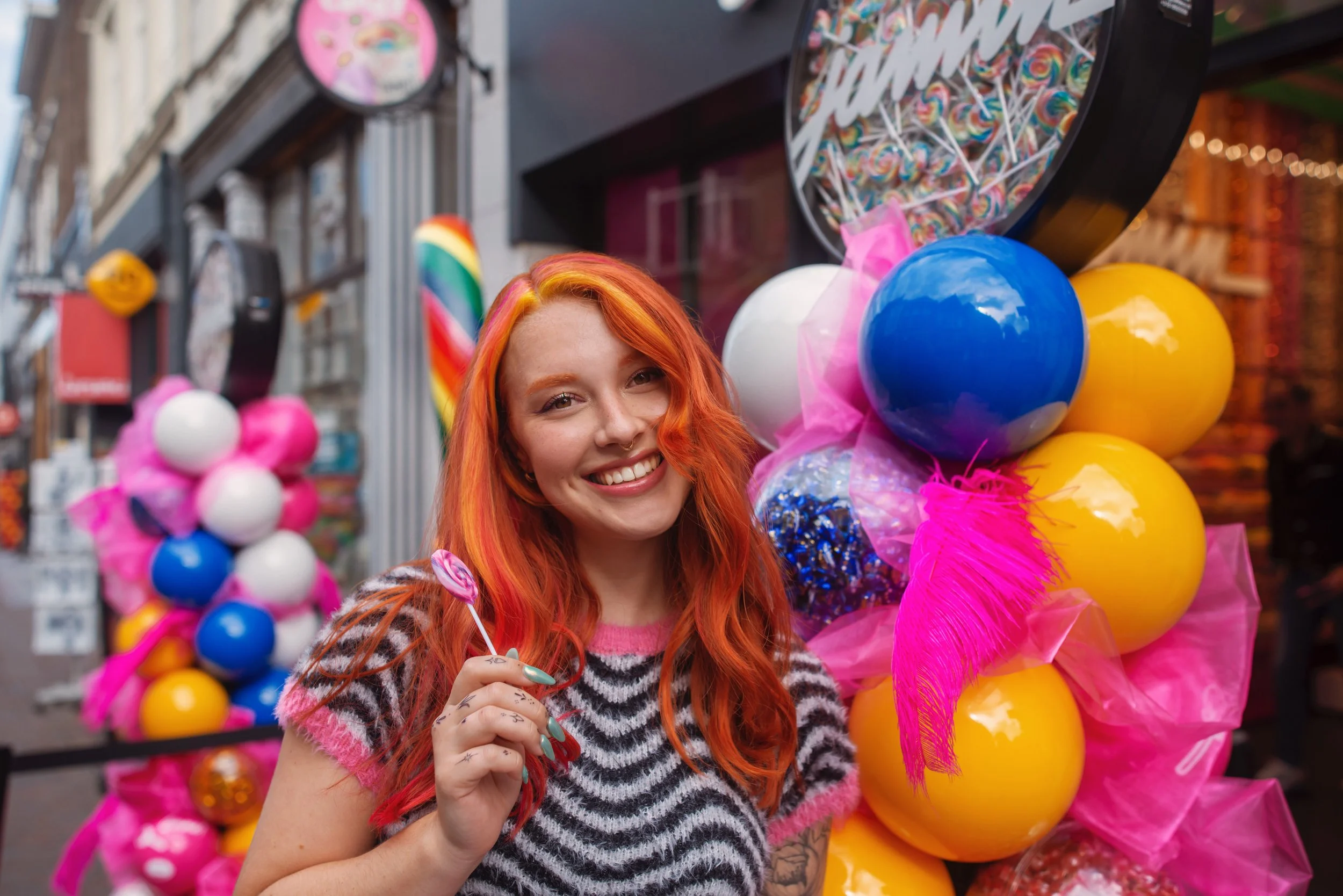 Dutch model with red hair and tattoos posing in front of the store with a big smile and a lollipop from the candy store Jamin