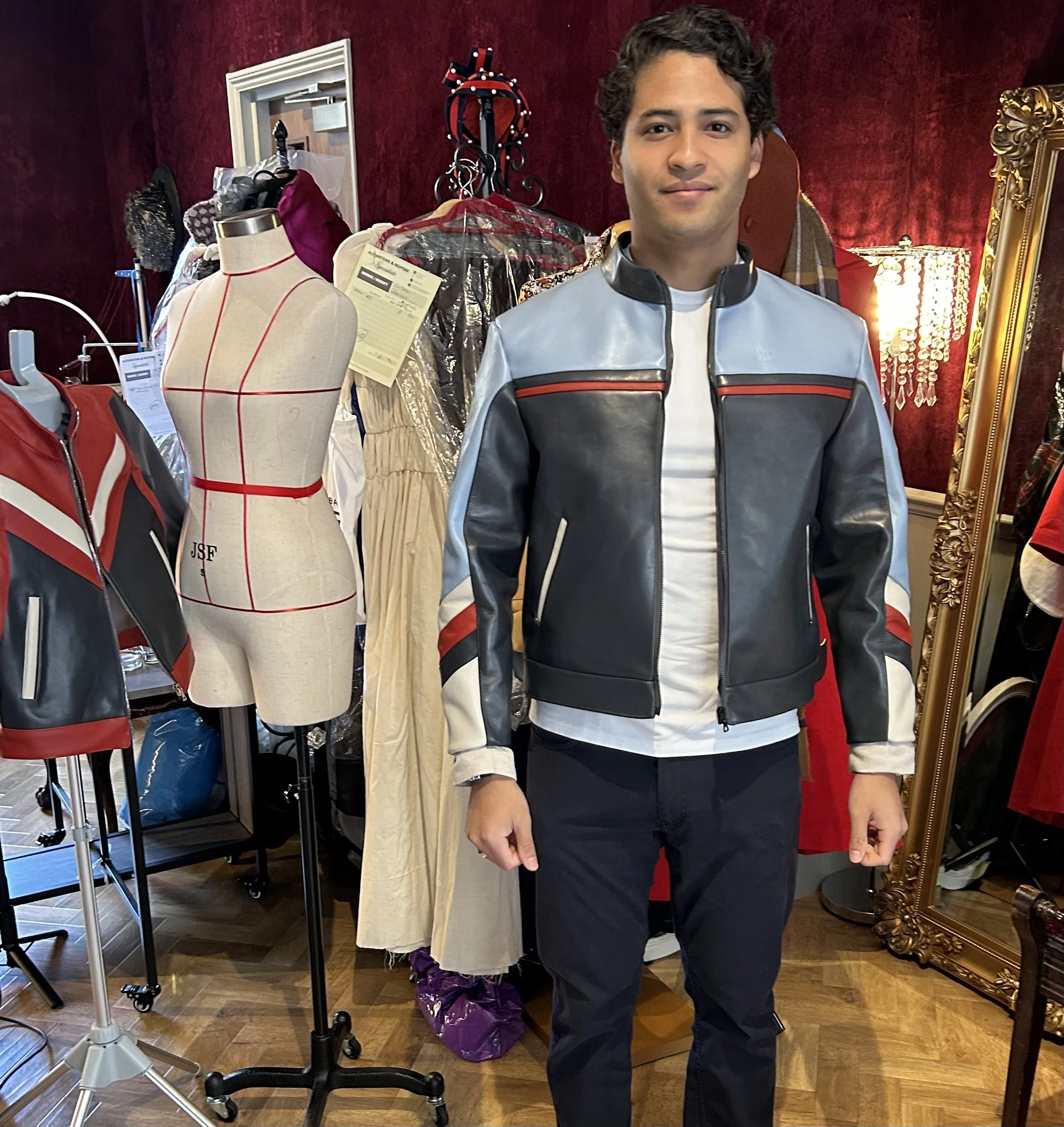 Man standing in costume store with mannequin, clothing racks, and mirror in the background.