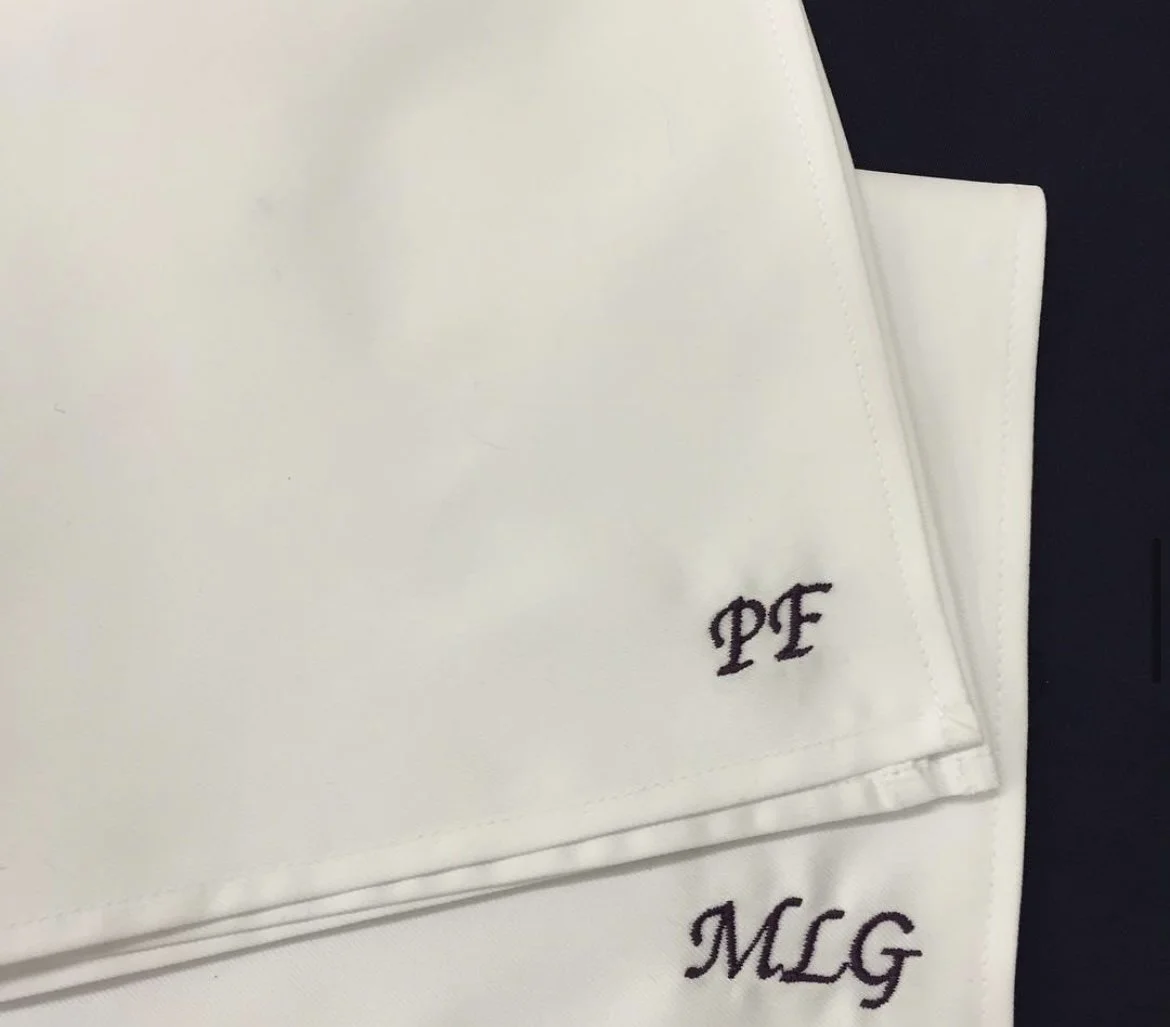 White cloth with black embroidered initials 'PE' and 'MLG'.