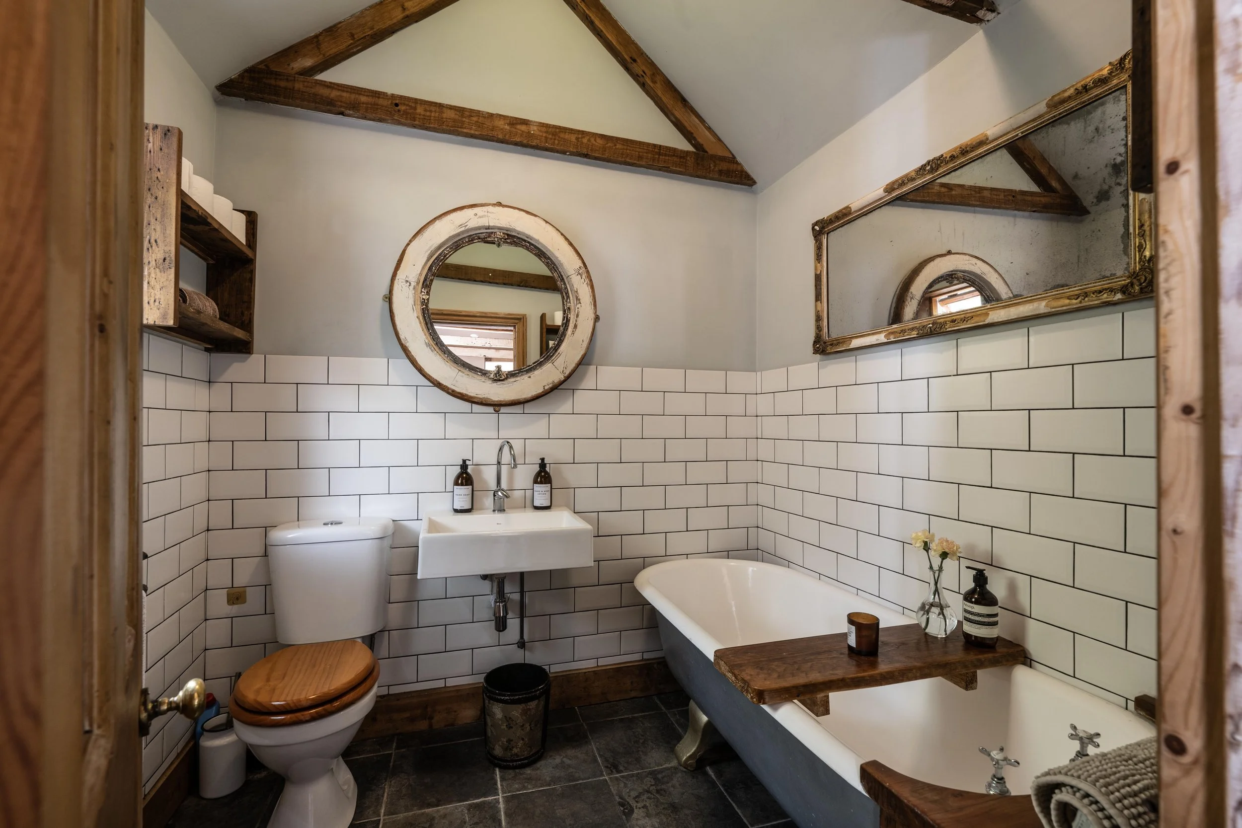 A large down stairs bathroom with the original roll top bath, vaulted ceilings and wooden beams.  