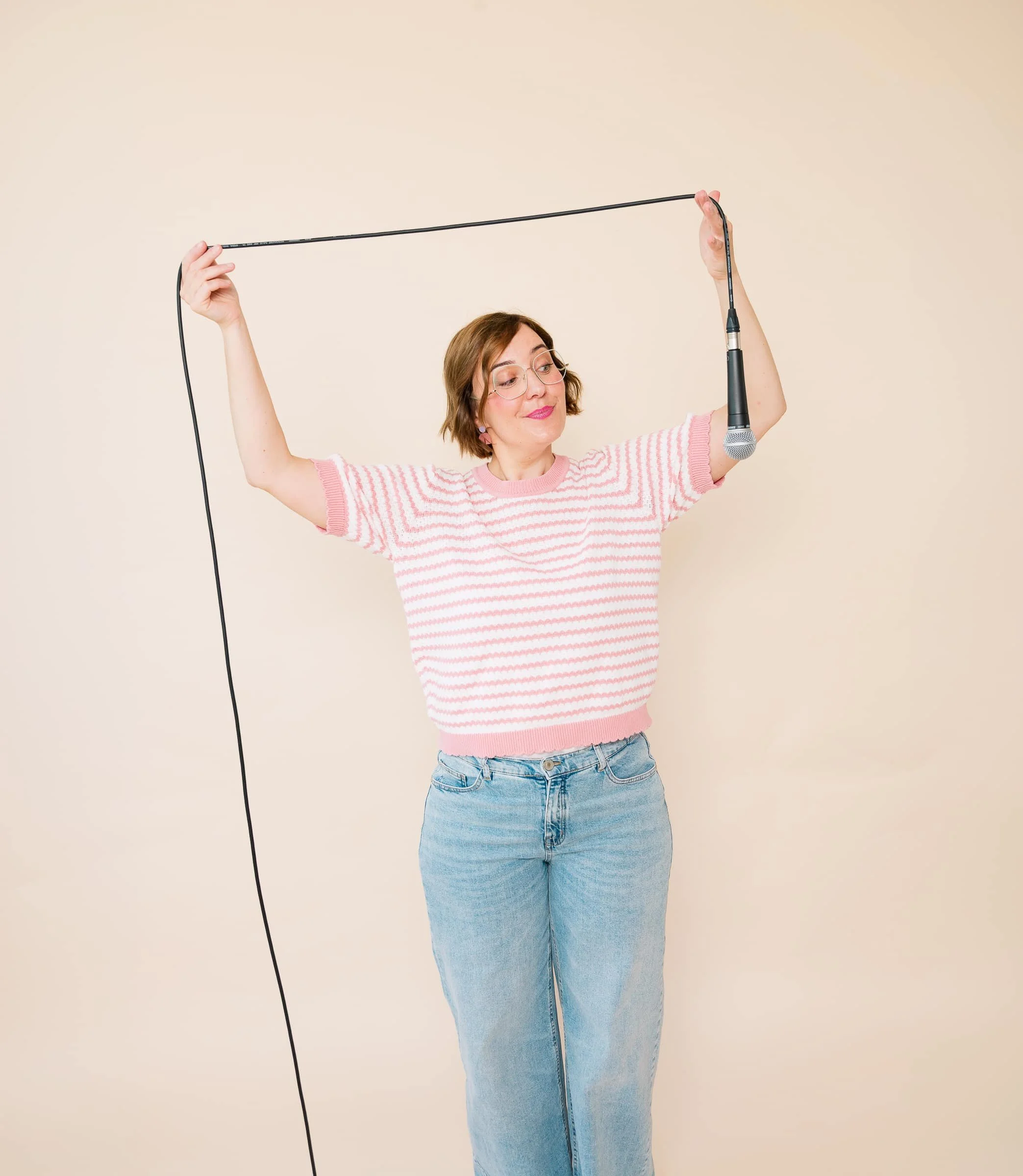 Portrait von Ina Kimmel, Gründerin von THERAPIEPAUSE®. Sie hält ein Podcastmikrofon mit einem langen Kabel über ihrem Kopf und schaut das Mikrofon lächelnd an.