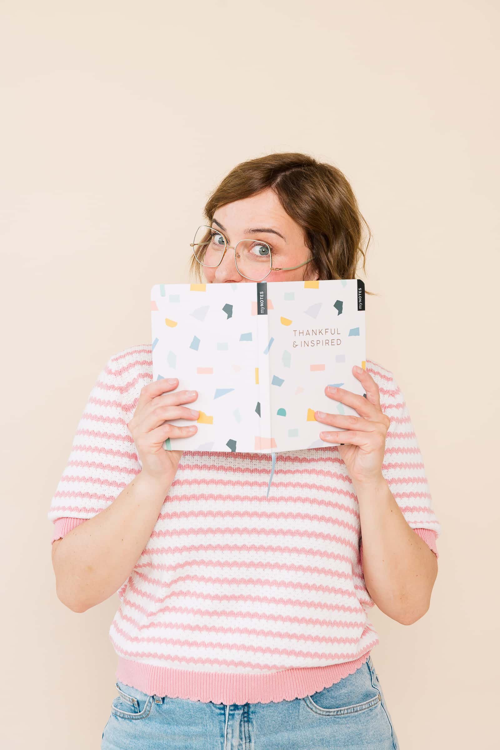 Portrait von Ina Kimmel, Gründerin und Coach bei THERAPIEPAUSE®, sie hält ein Notizbuch vor ihren Mund und schaut neugierig darüber