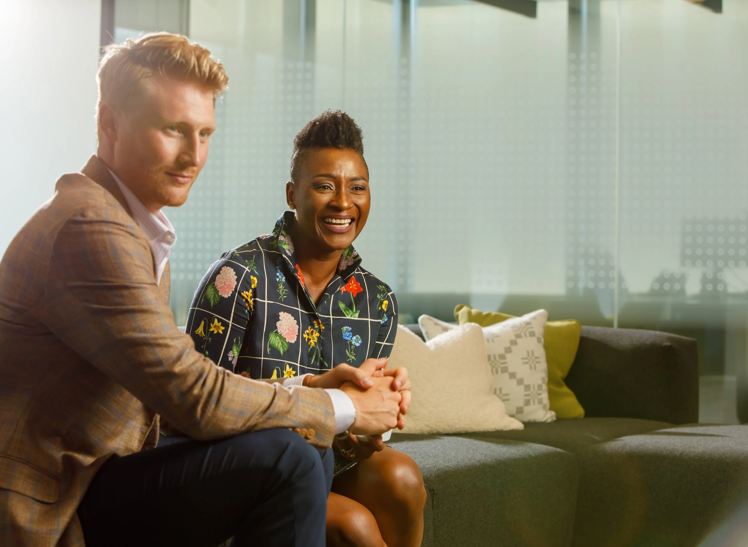A professional man and professional woman sitting in an office lobby chatting