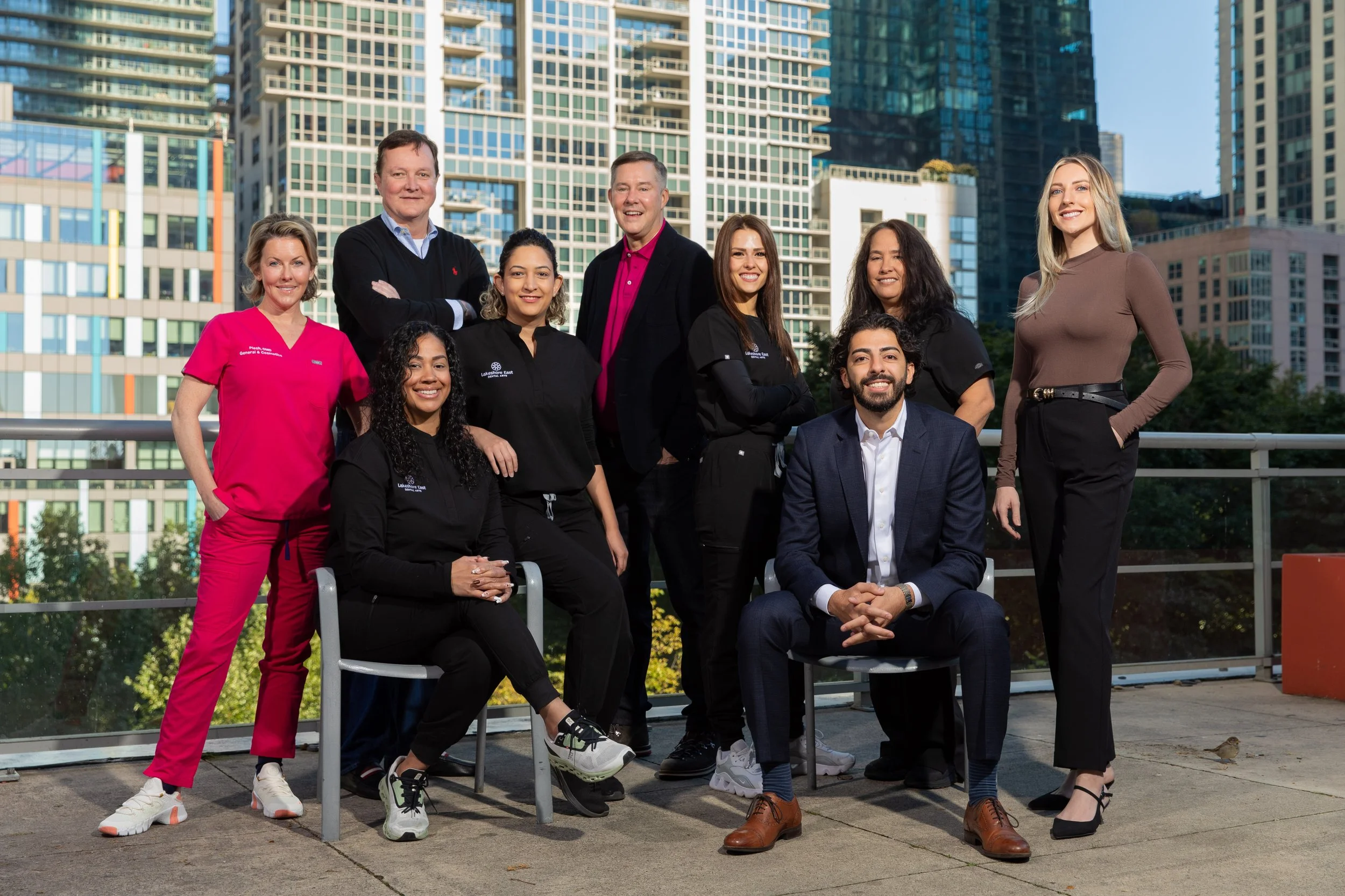 Group of nine diverse professionals posing outdoors in an urban area with tall buildings in the background.