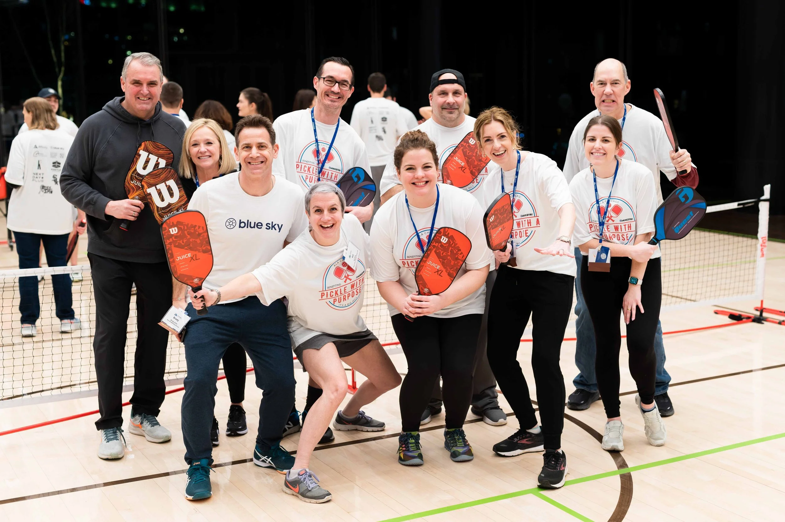 Group of people holding pickleball paddles on an indoor court, smiling for the camera