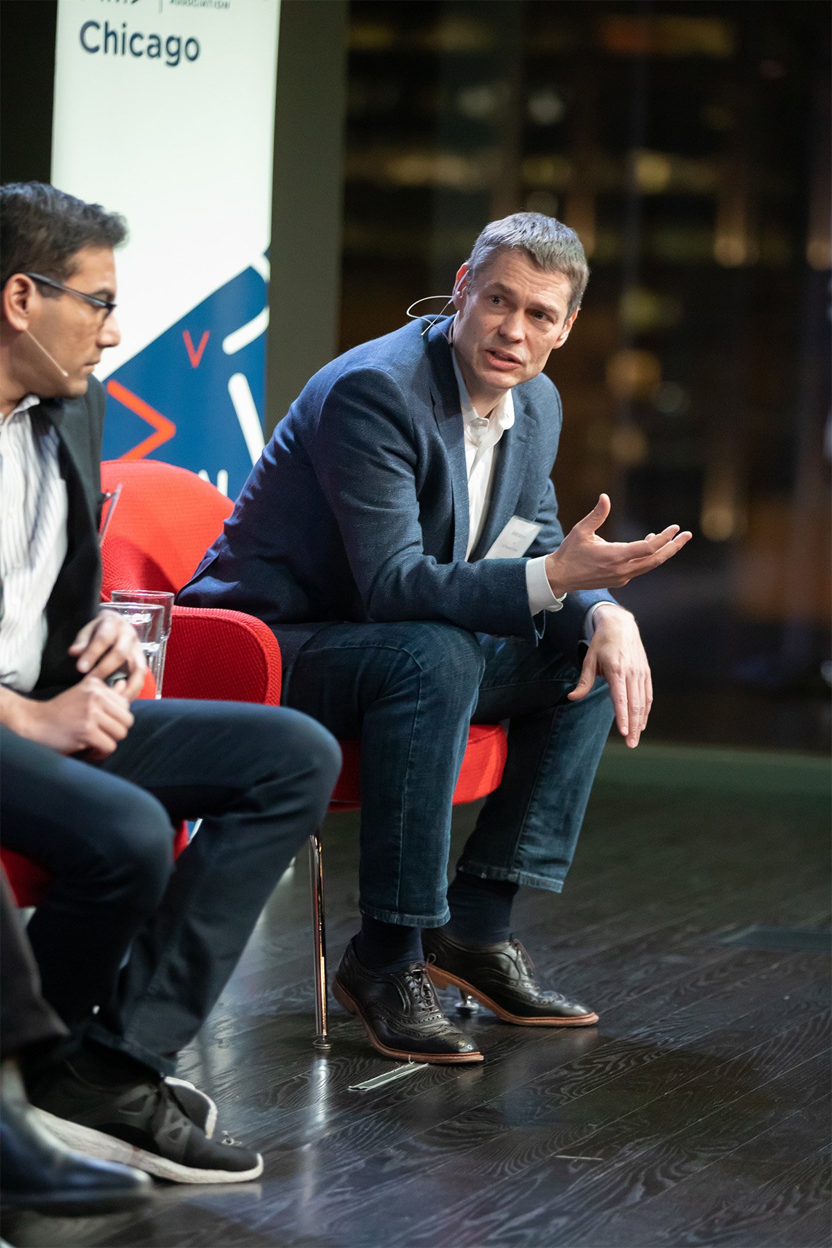 Two men seated on stage with a backdrop that reads 'Chicago,' engaged in conversation at a professional event.