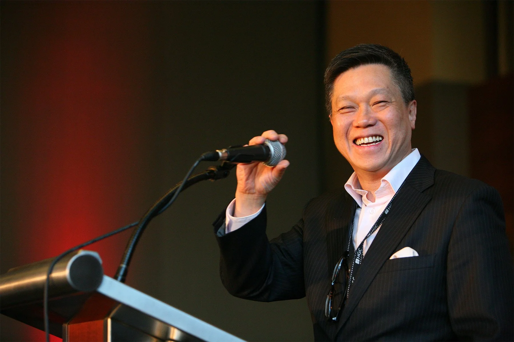 Man in a suit smiling while holding a microphone at a conference or event.