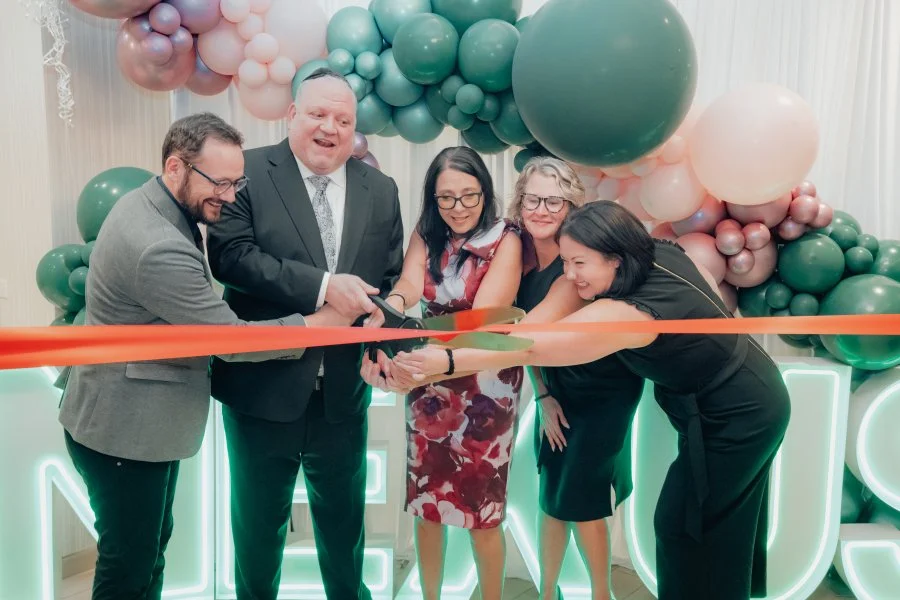 five people cutting a large ribbon at an event
