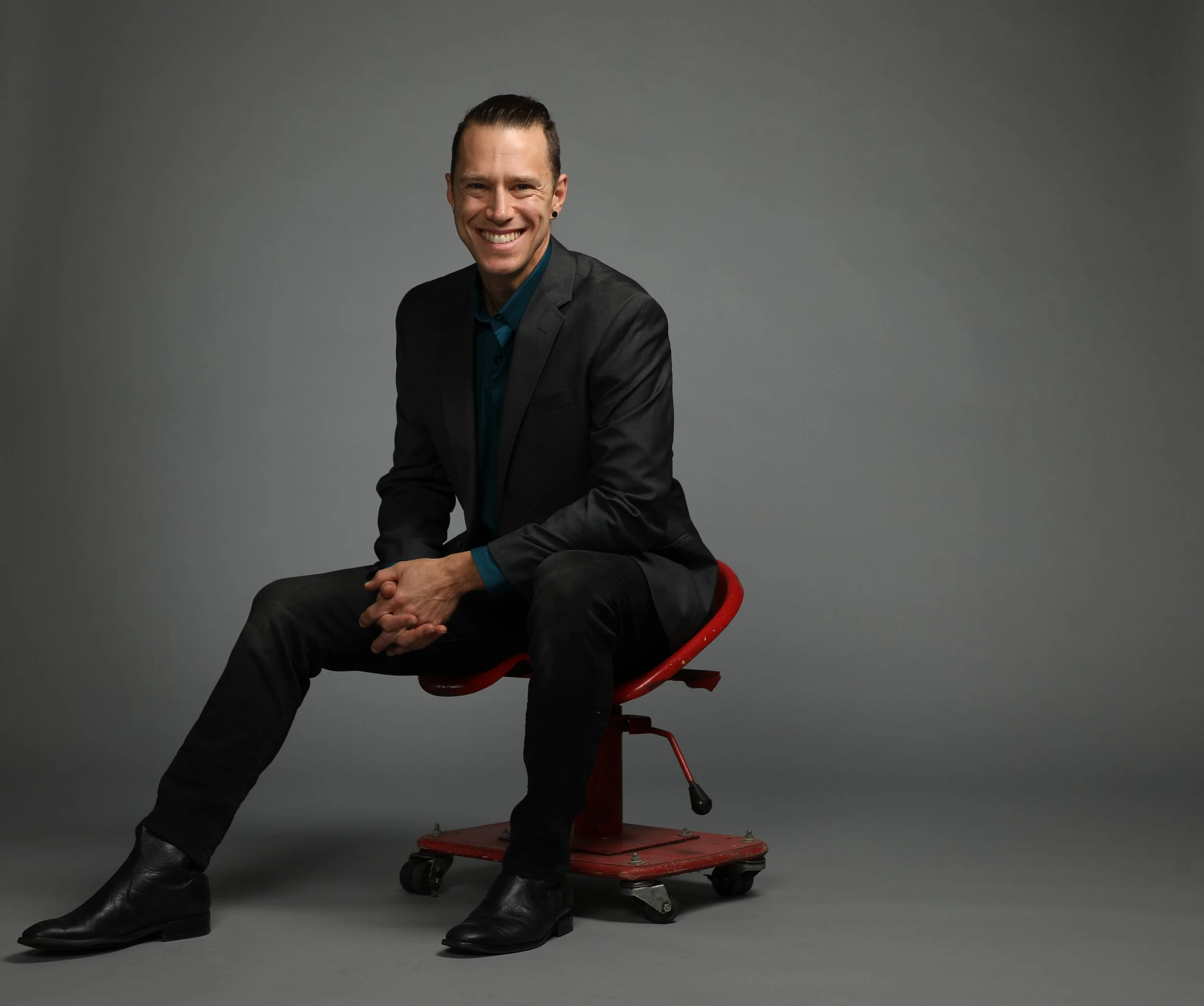 portrait of a professional man sitting on a red stool in front of a gray background