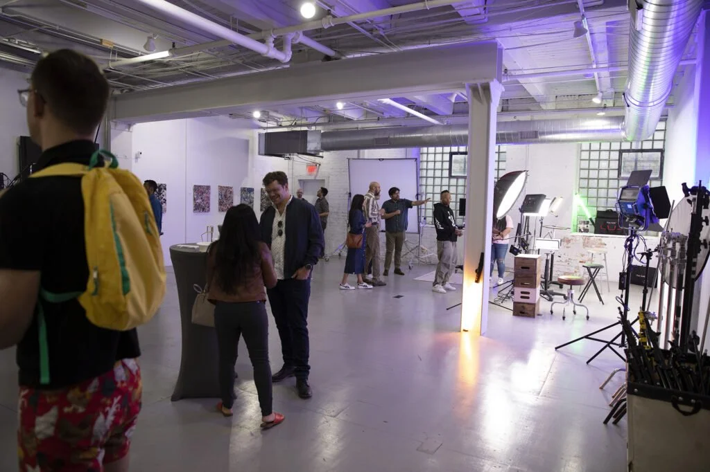 People preparing a photography studio with lighting and camera equipment in a modern industrial space, some are involved in setup while others engage in conversation.