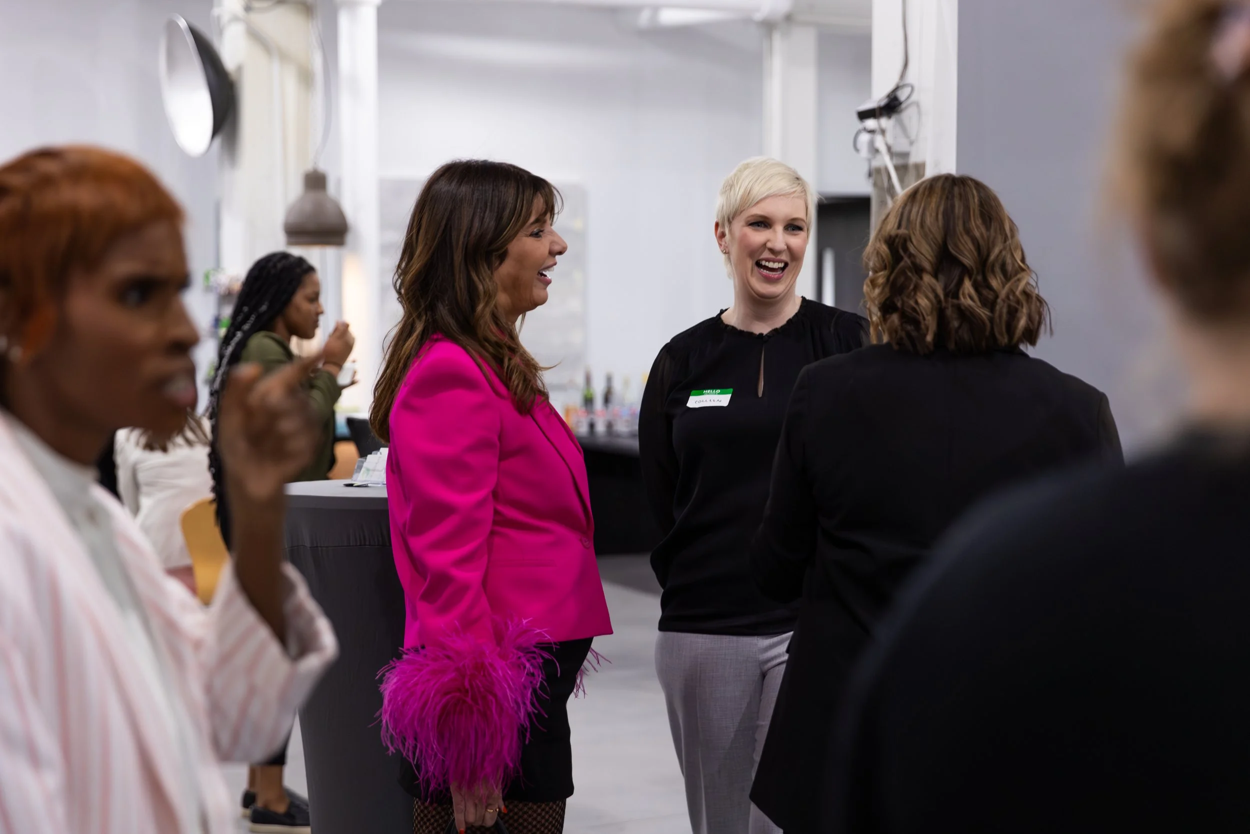 A group of women at a social gathering, laughing and talking in an indoor setting.