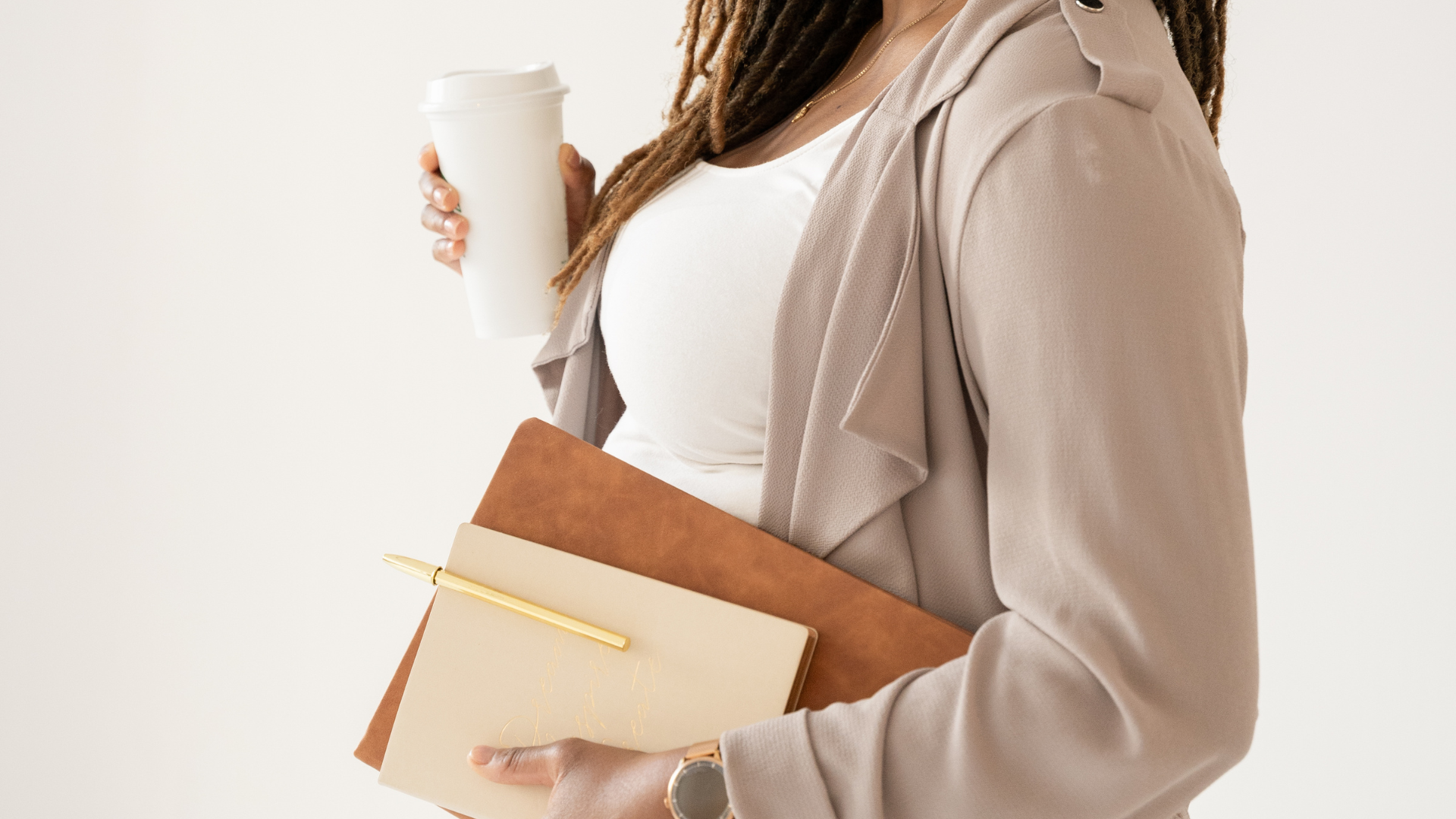 A midlife woman holding a cup of coffee in one hand and a folder and notebook with pen in the other, ready to take on the next meeting or day with confidence.