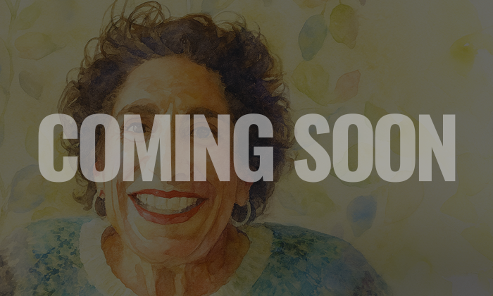 A smiling elderly woman with curly hair, wearing a light-colored top, with a blurred colorful background.