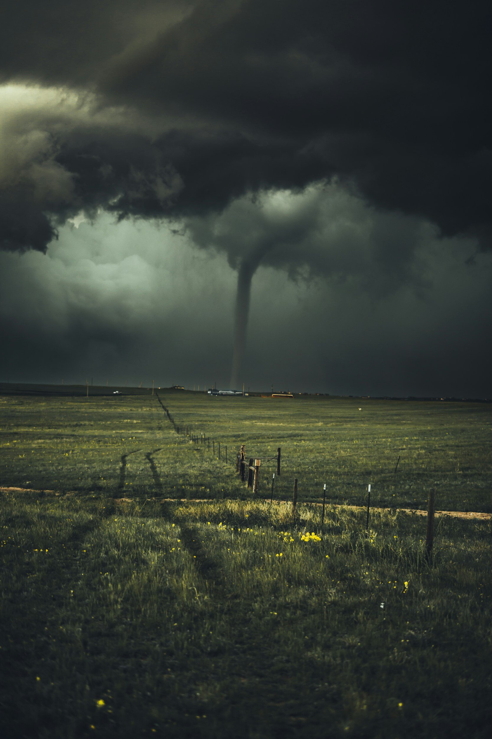 A tornado touching down in an open field under dark storm clouds.