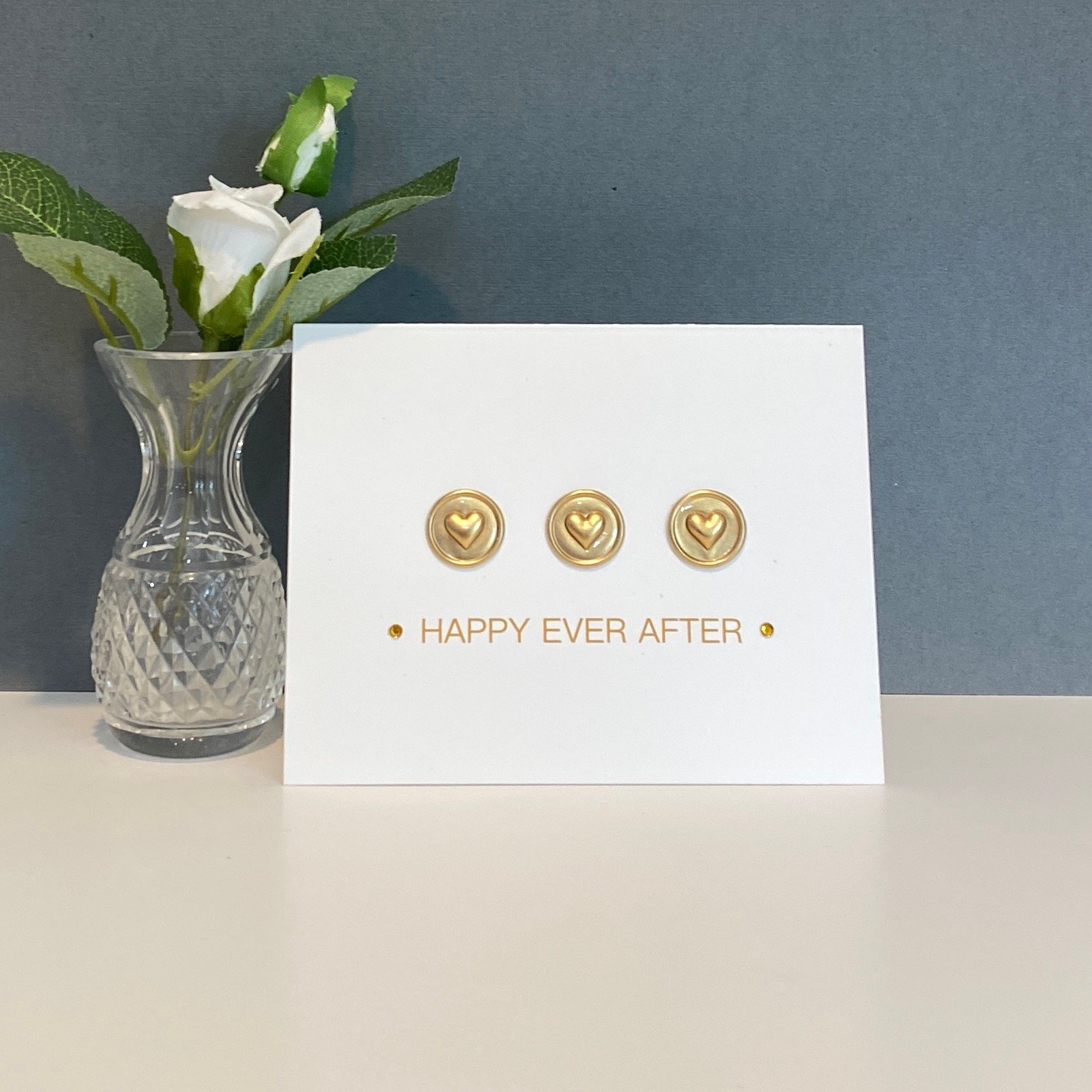 Card with hearts and vase with rose on desk.