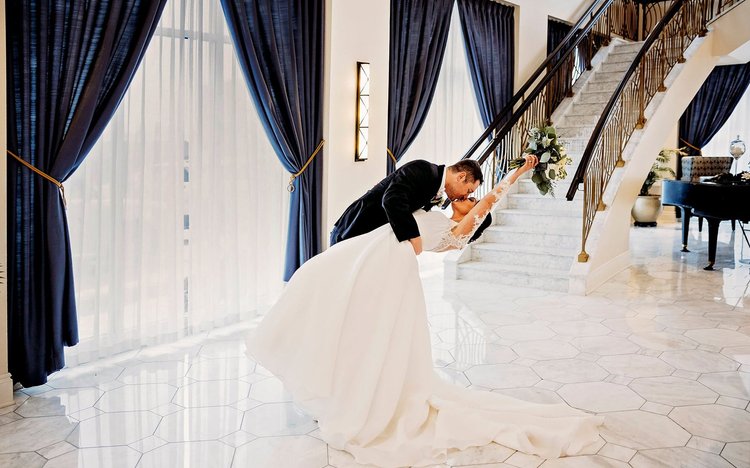 Bride and groom share a kiss at the foot of a sweeping white staircase