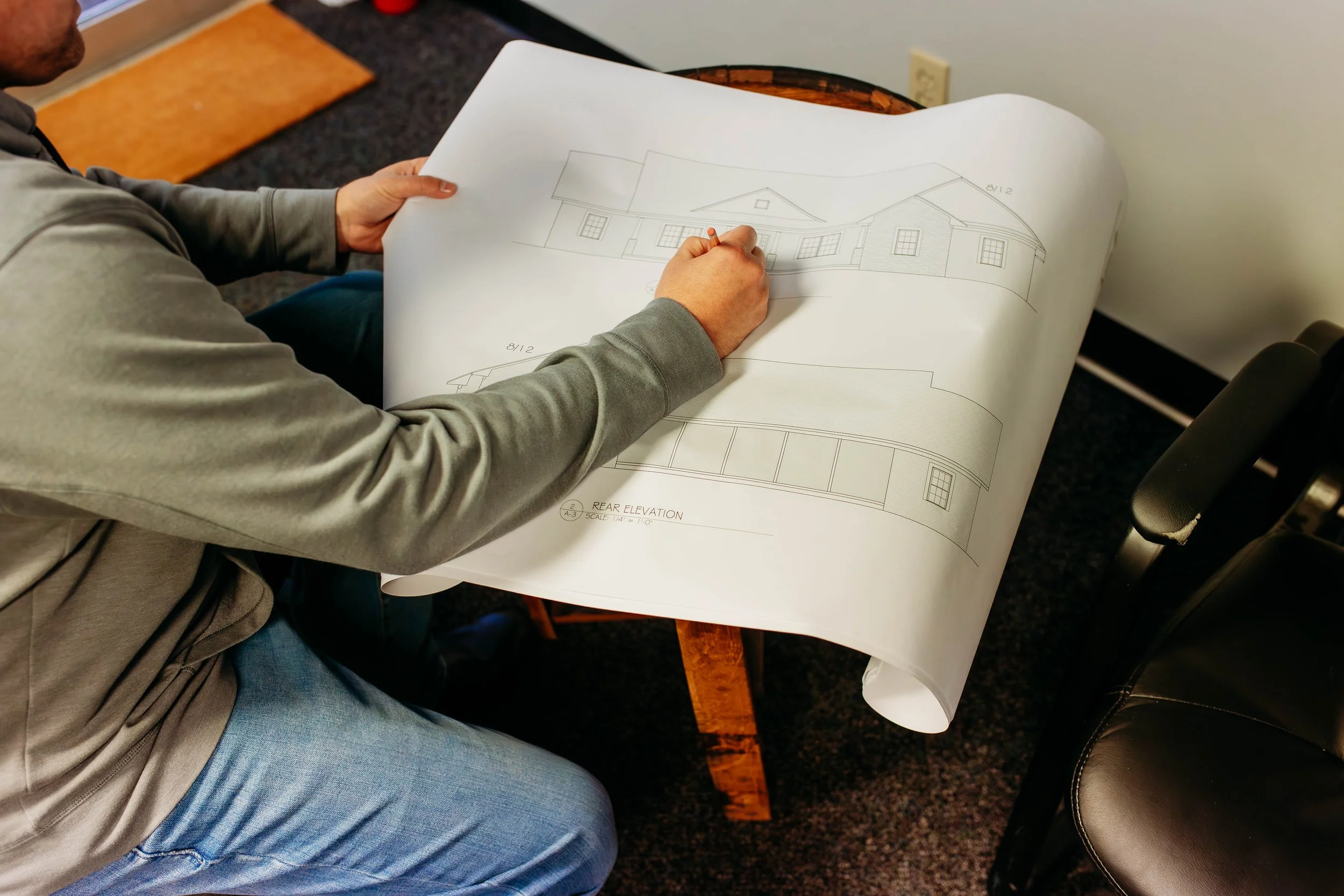 Person examining architectural blueprints at a table, featuring building elevation drawings.