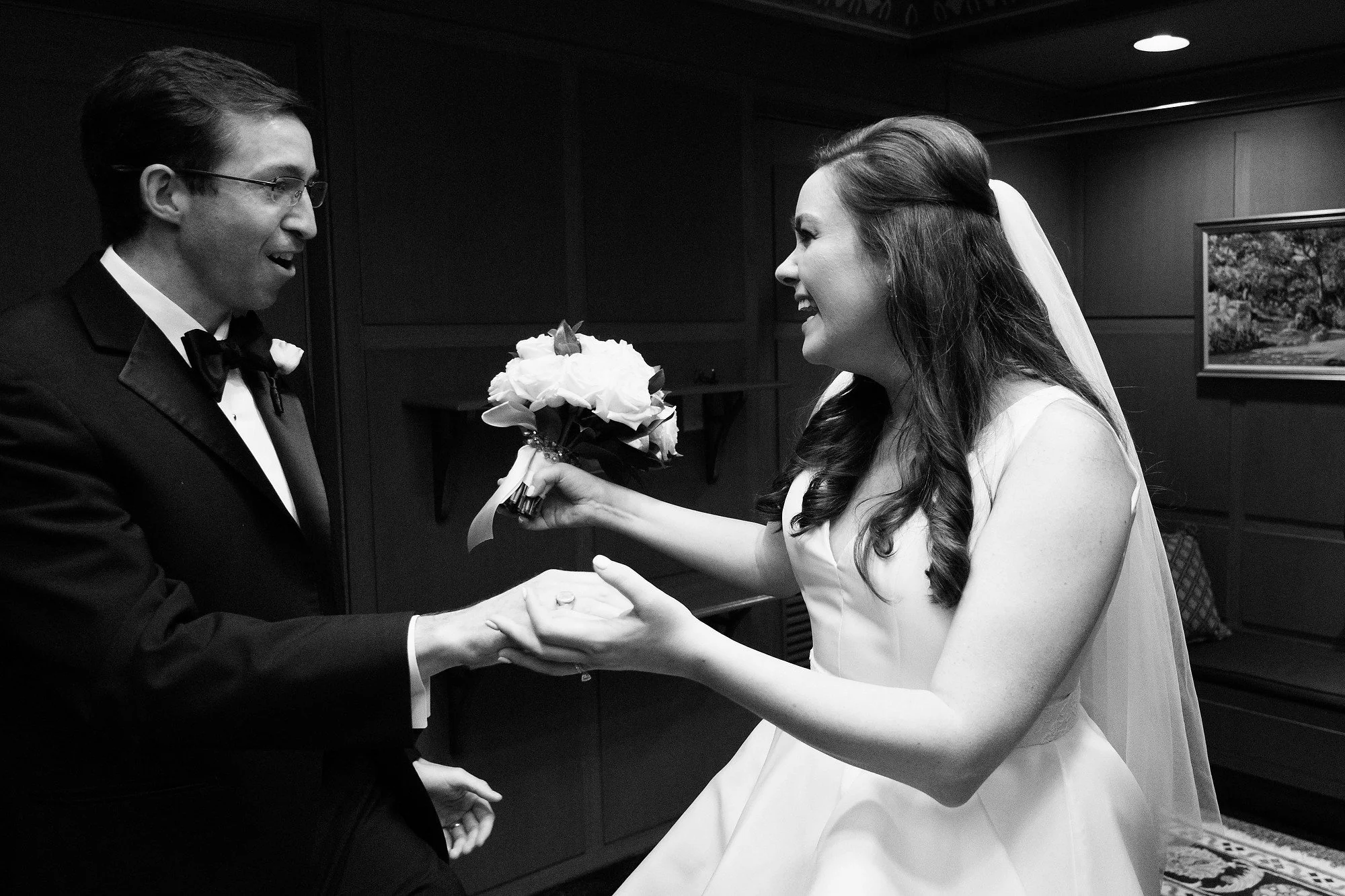 A bride and groom smiling at each other during their wedding, with the bride holding a bouquet of flowers.