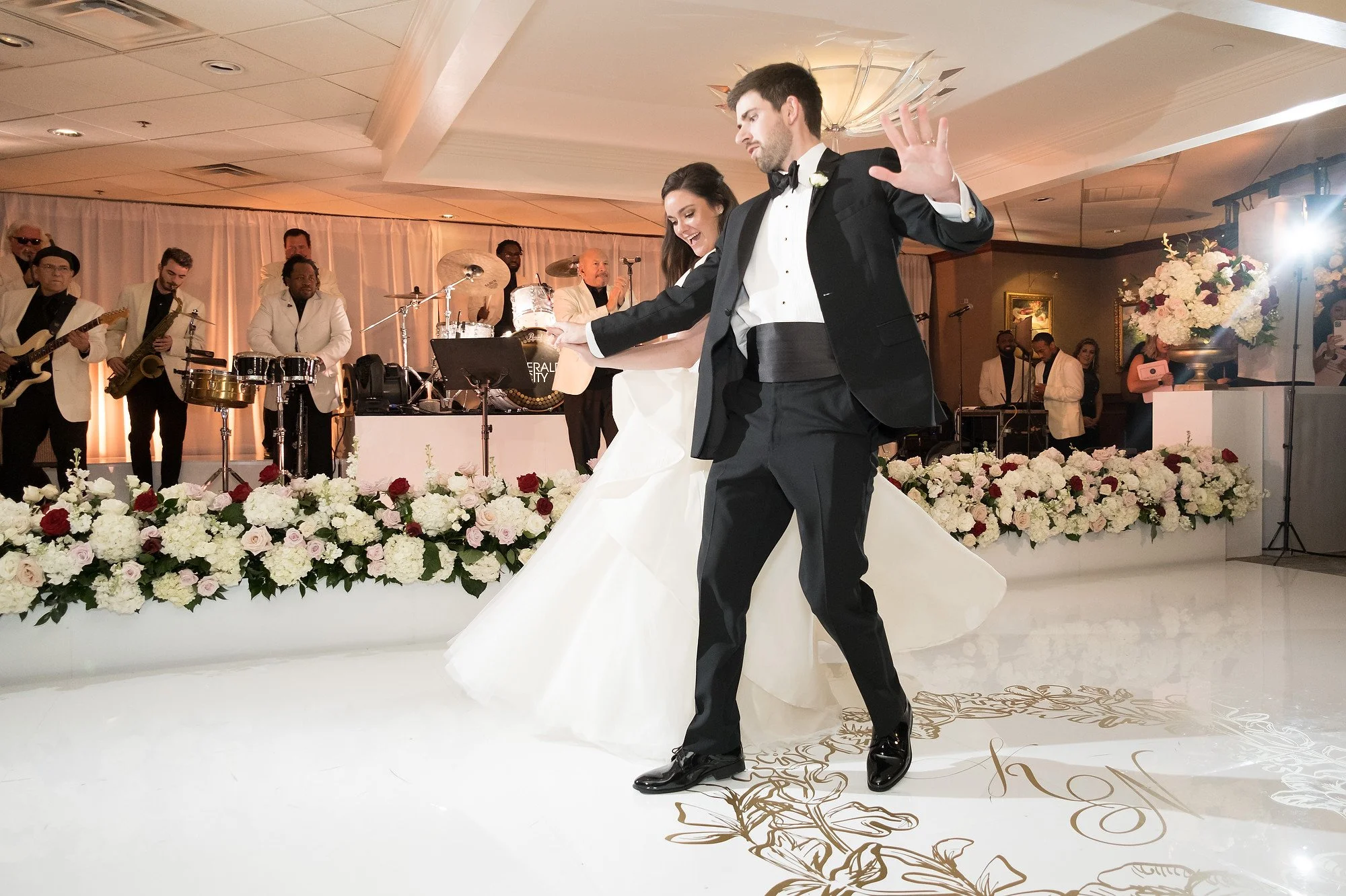 Couple dancing at their wedding reception with a band playing live music in the background, surrounded by floral arrangements.