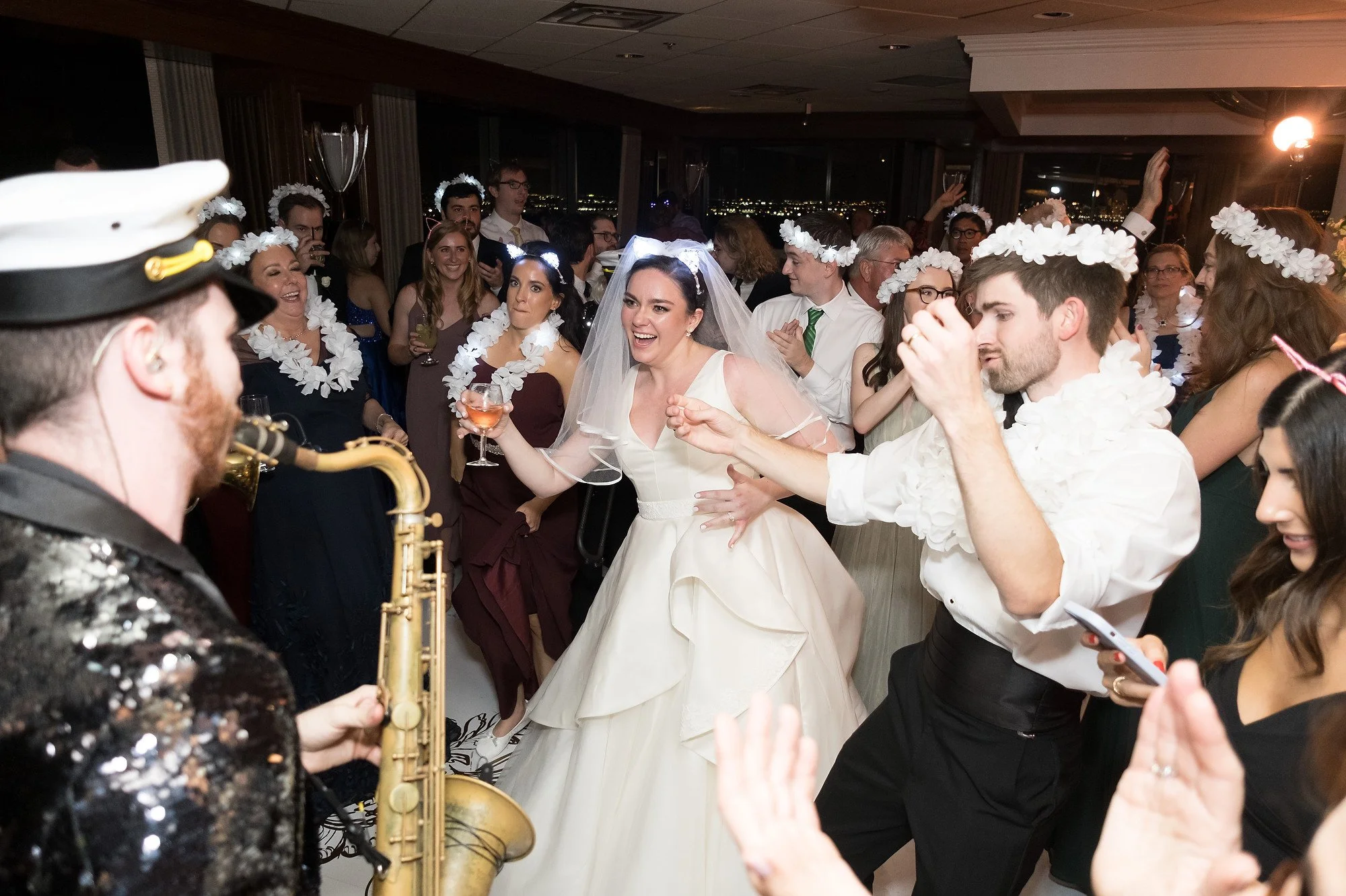 People dancing and celebrating at a wedding reception, with a musician playing saxophone in the foreground.