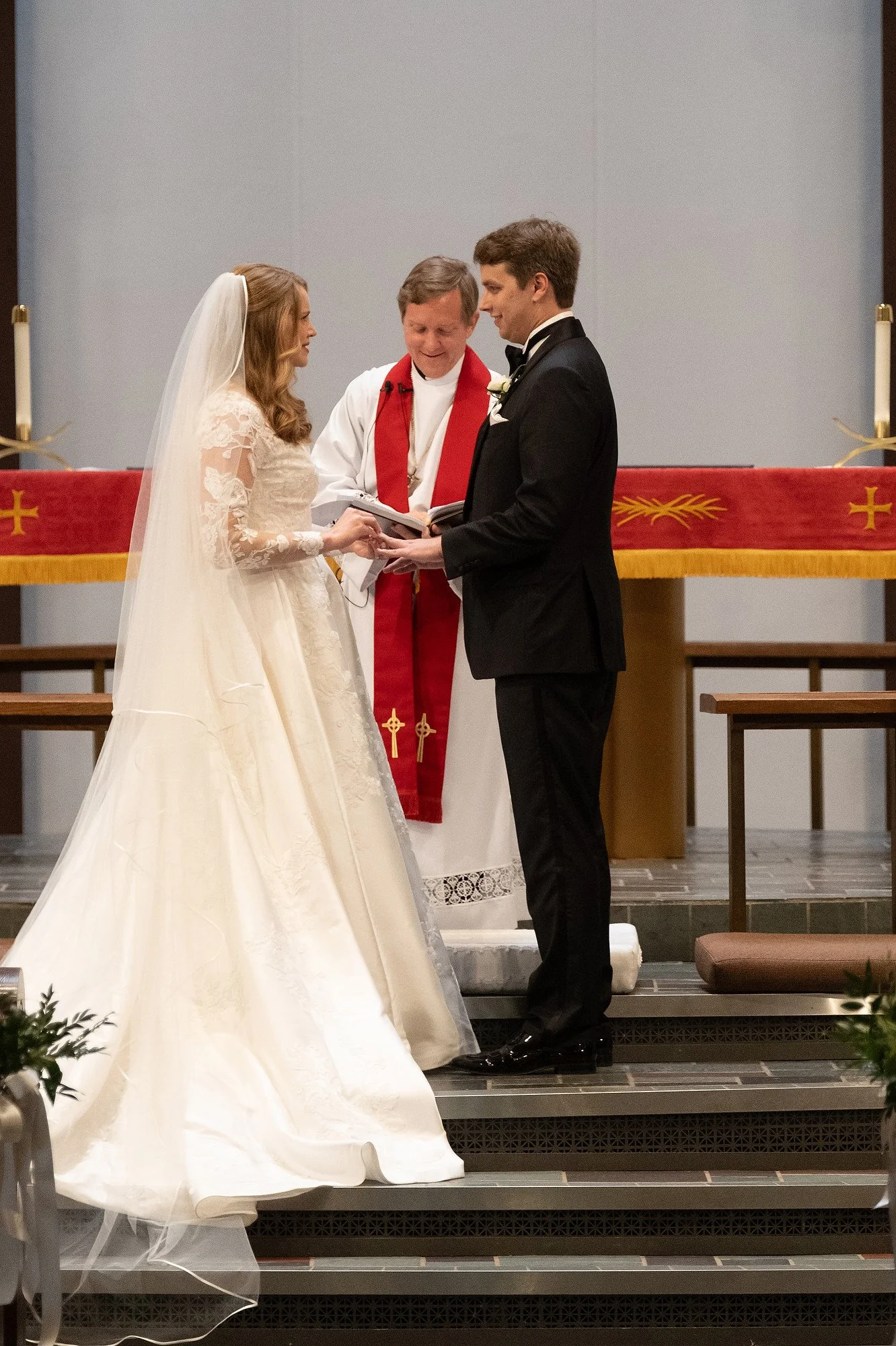 A bride and groom holding hands during a wedding ceremony with a priest officiating in a church.