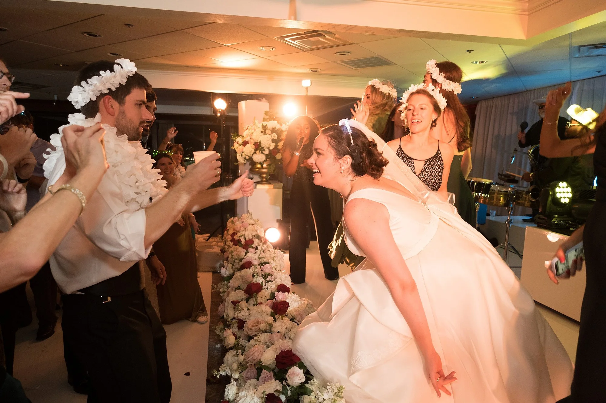 Wedding reception with the bride and groom dancing, surrounded by friends, floral decorations, and colorful lighting.