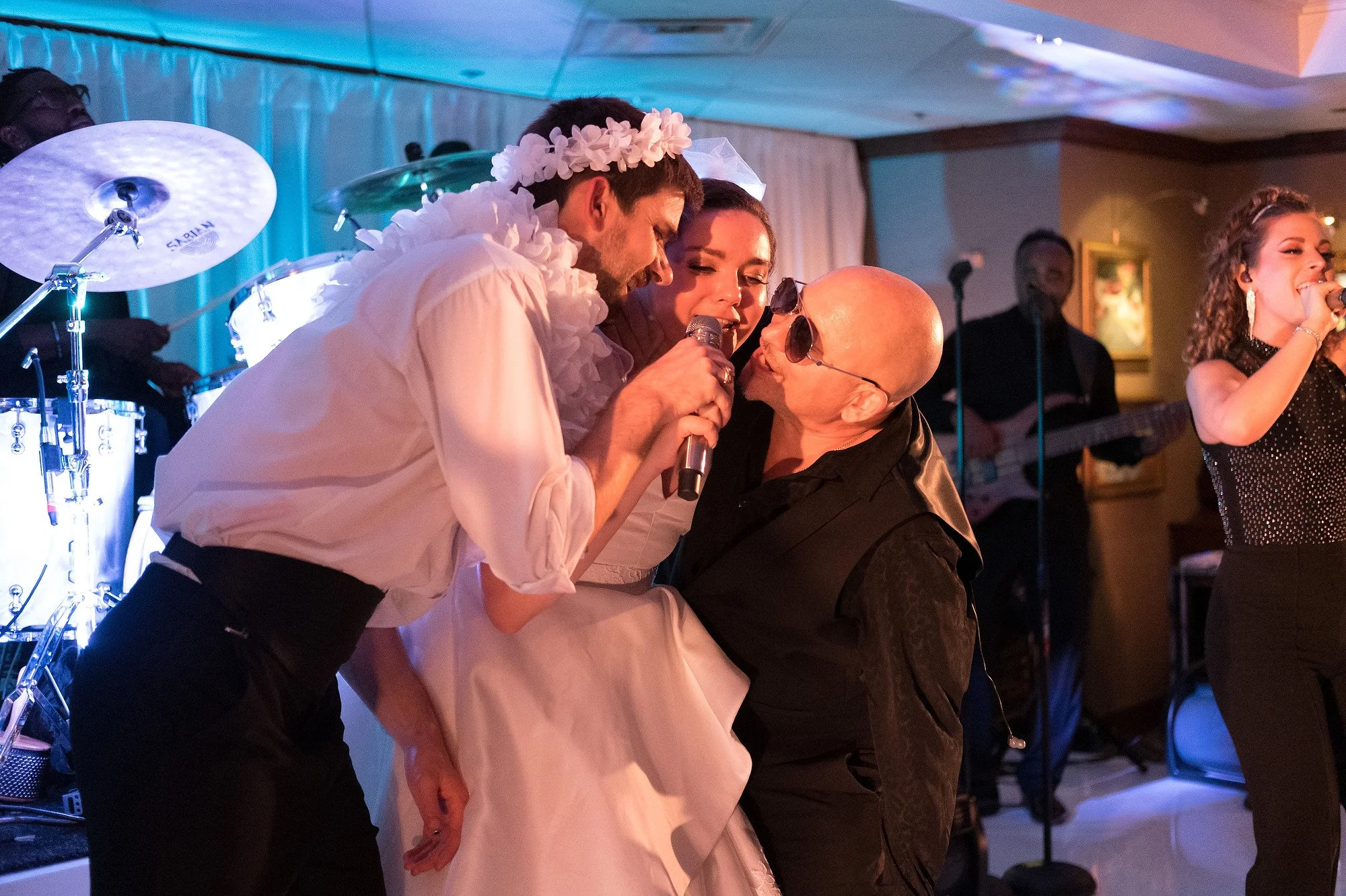 A group of performers singing karaoke at a celebration, with a band playing in the background.