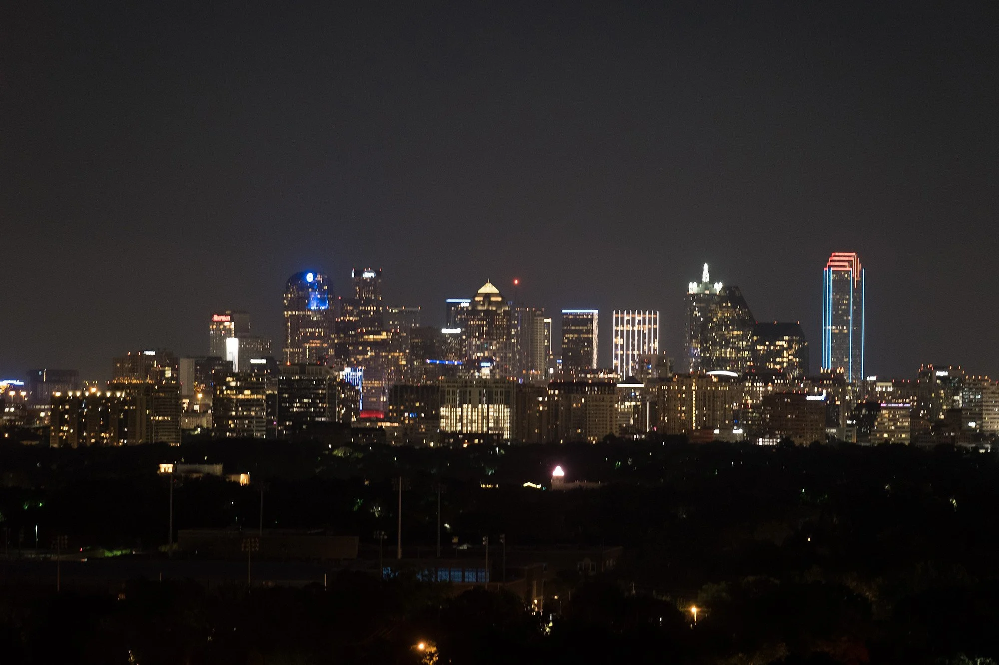 Night view of downtown Dallas skyline illuminated with various lit skyscrapers against dark sky