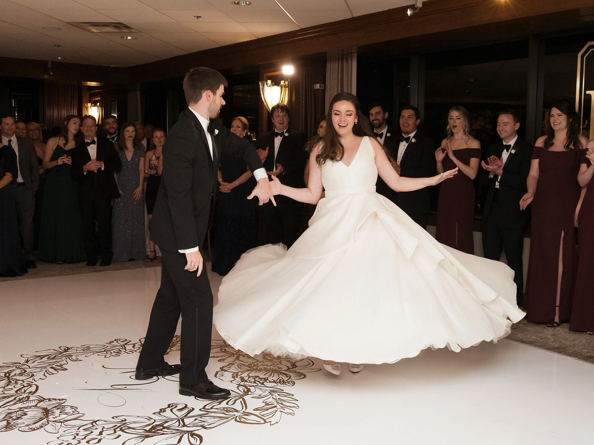 A bride and groom dancing at their wedding reception with guests watching and clapping in the background.
