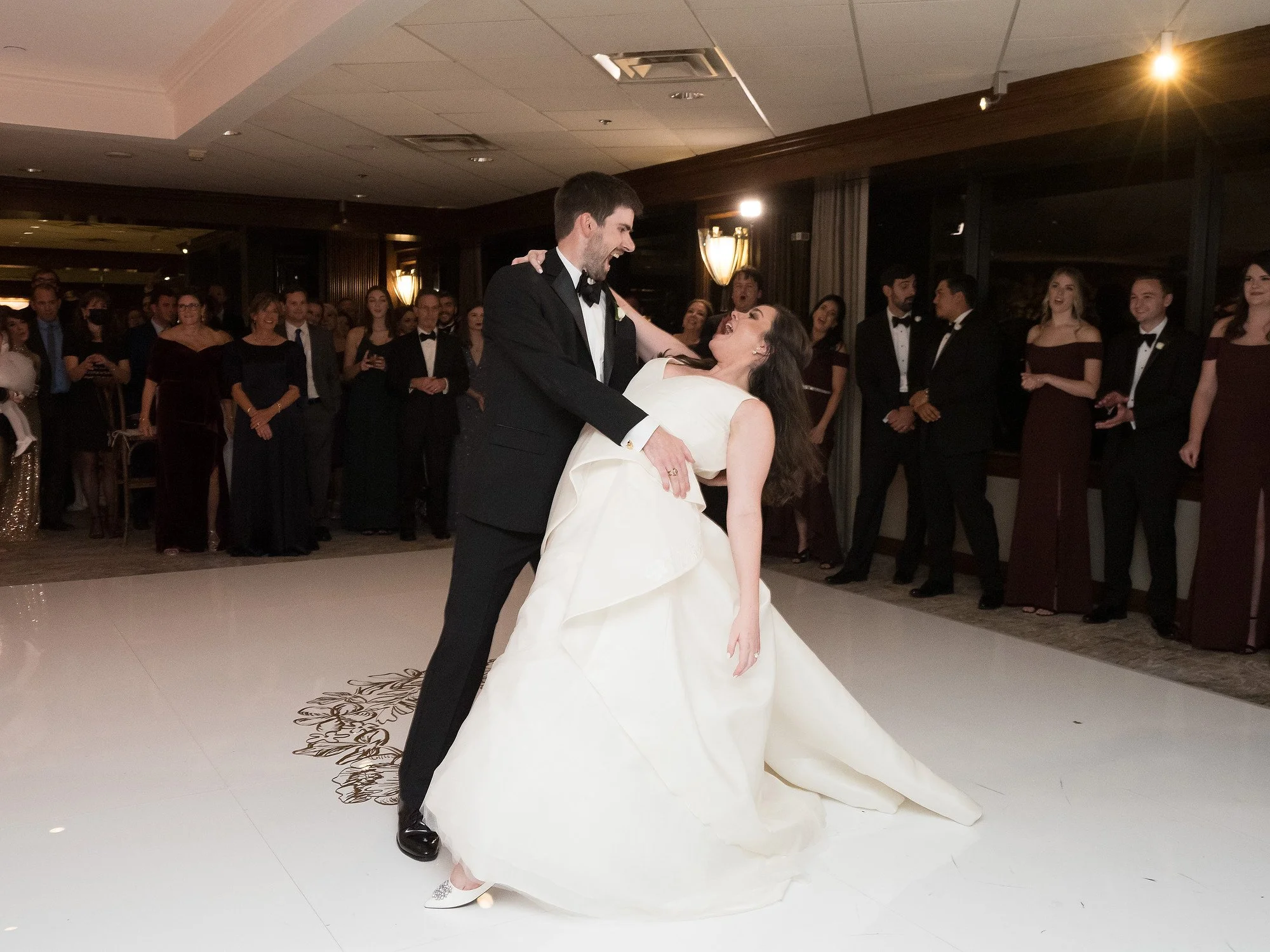 Bride and groom dancing at wedding reception with guests watching in the background.