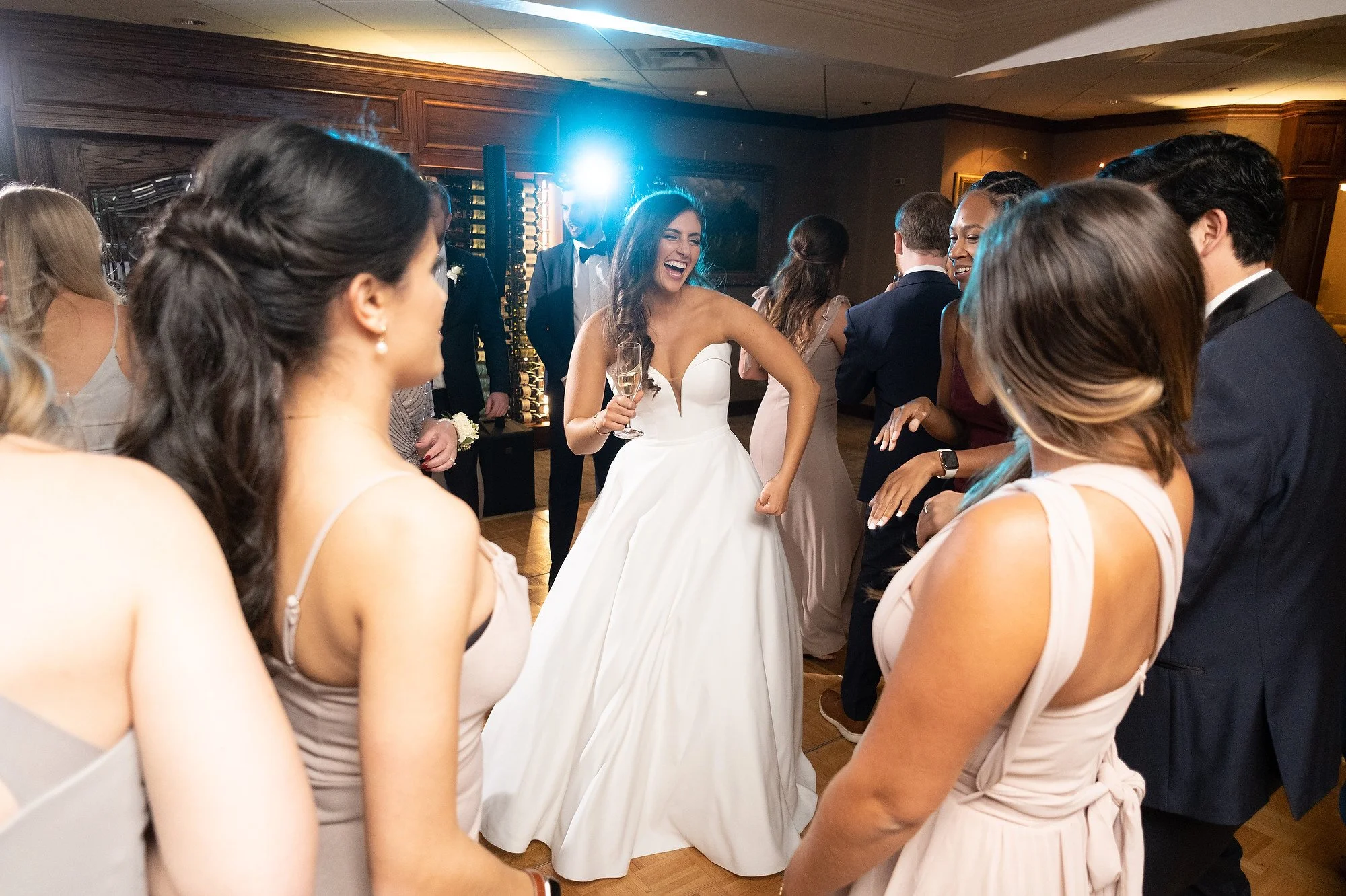 A bride in a white wedding dress is dancing and laughing with friends at a wedding reception.
