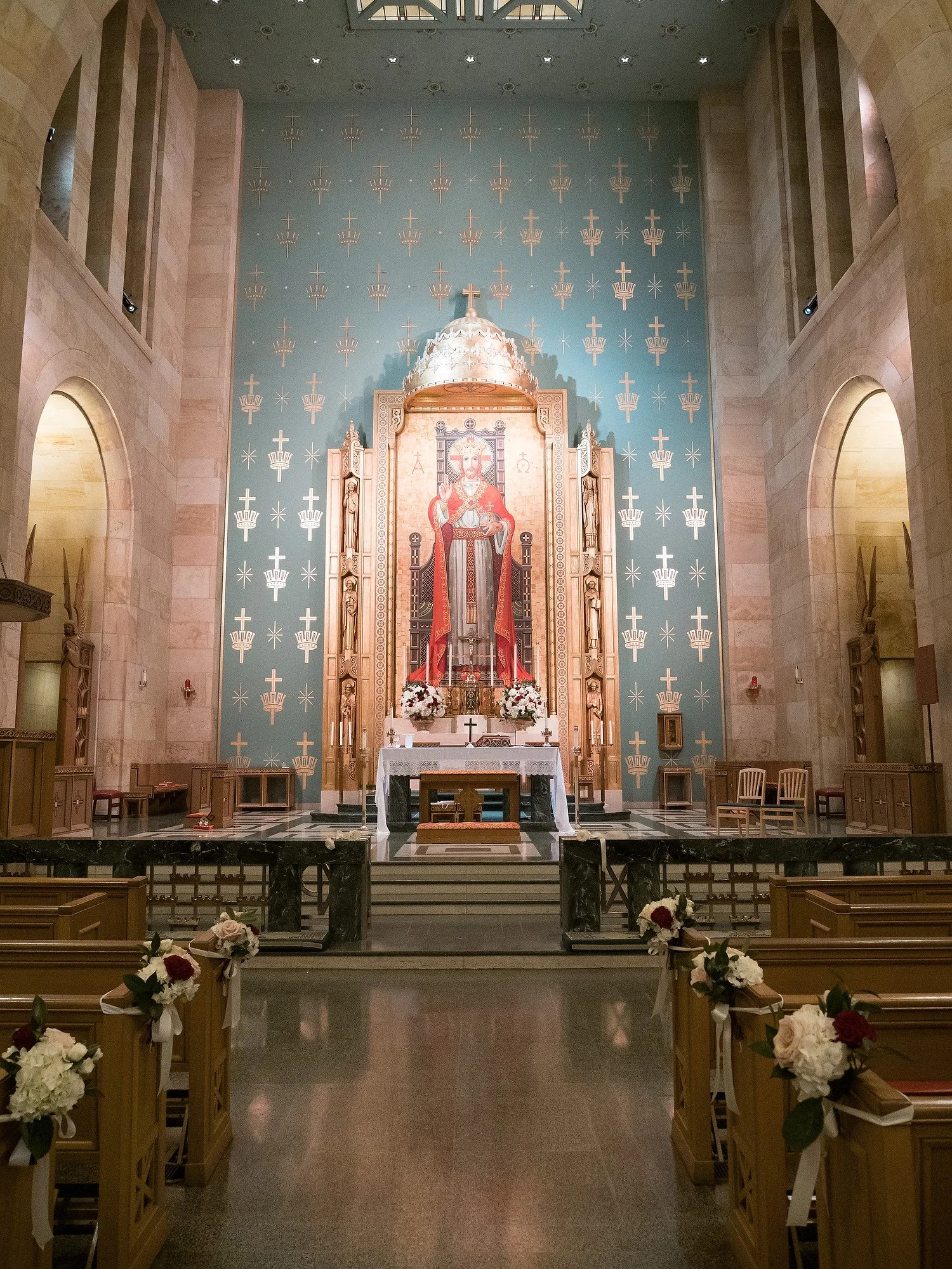 Interior of a church altar decorated with flowers, a large icon of a saint or religious figure, and gold accents. The pews are adorned with white and red flowers tied with ribbons.