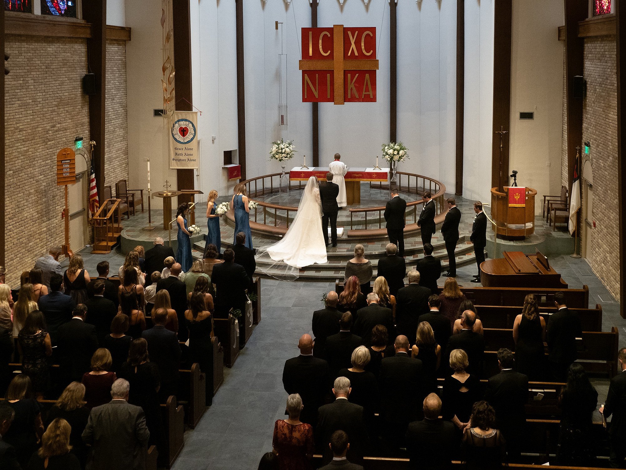 A wedding ceremony in a church with a bride and groom standing at the altar, surrounded by bridesmaids, groomsmen, and congregation members.