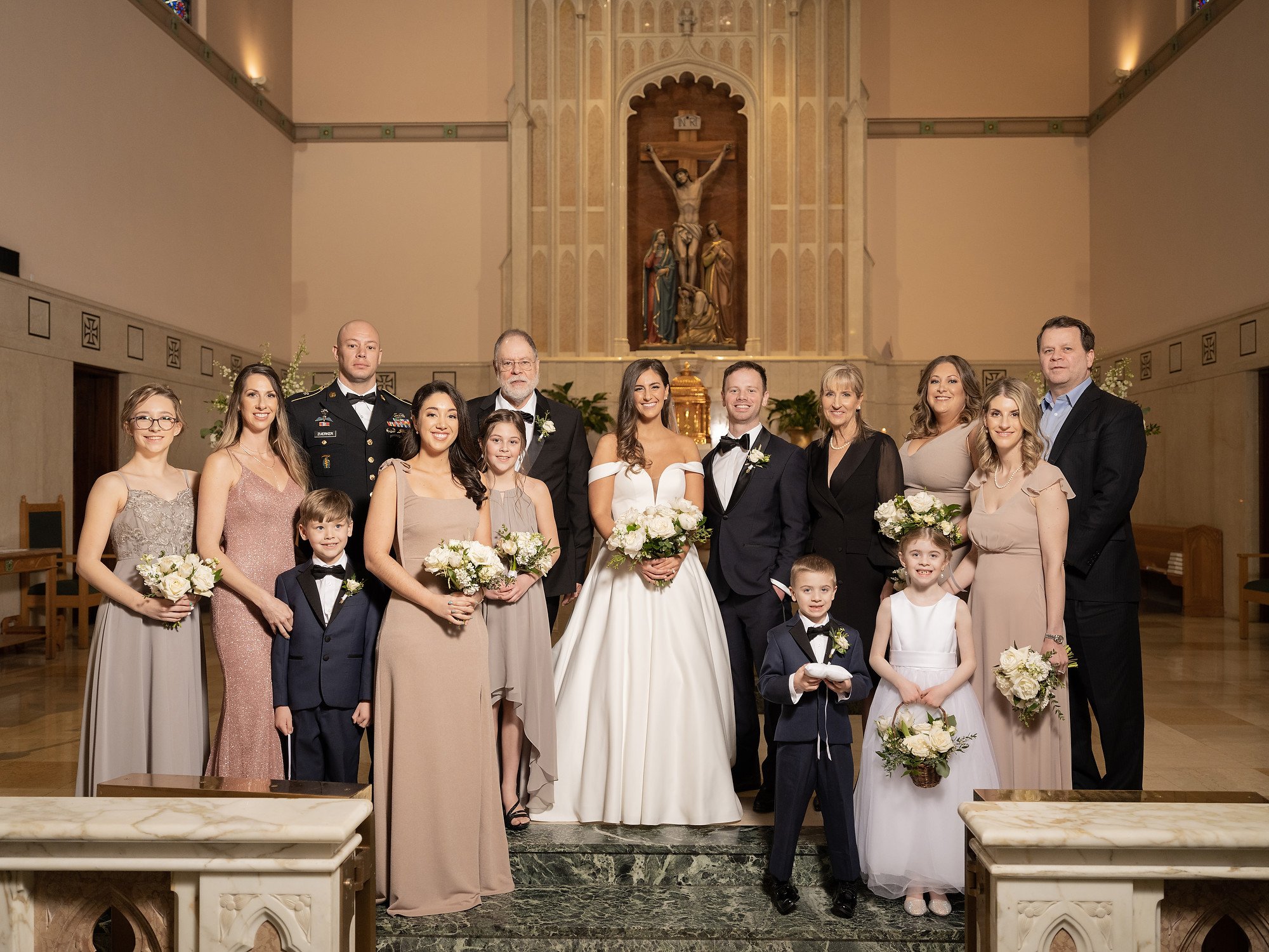 Group of wedding party members, including bride and groom, family and friends, standing inside a church near the altar, posing for a photo.