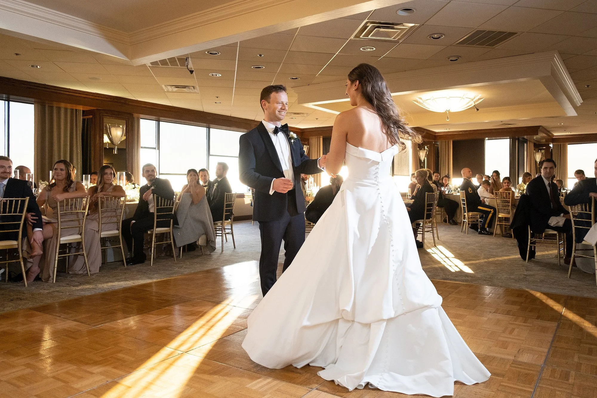 A bride and groom dancing during their wedding reception with guests seated at tables in the background