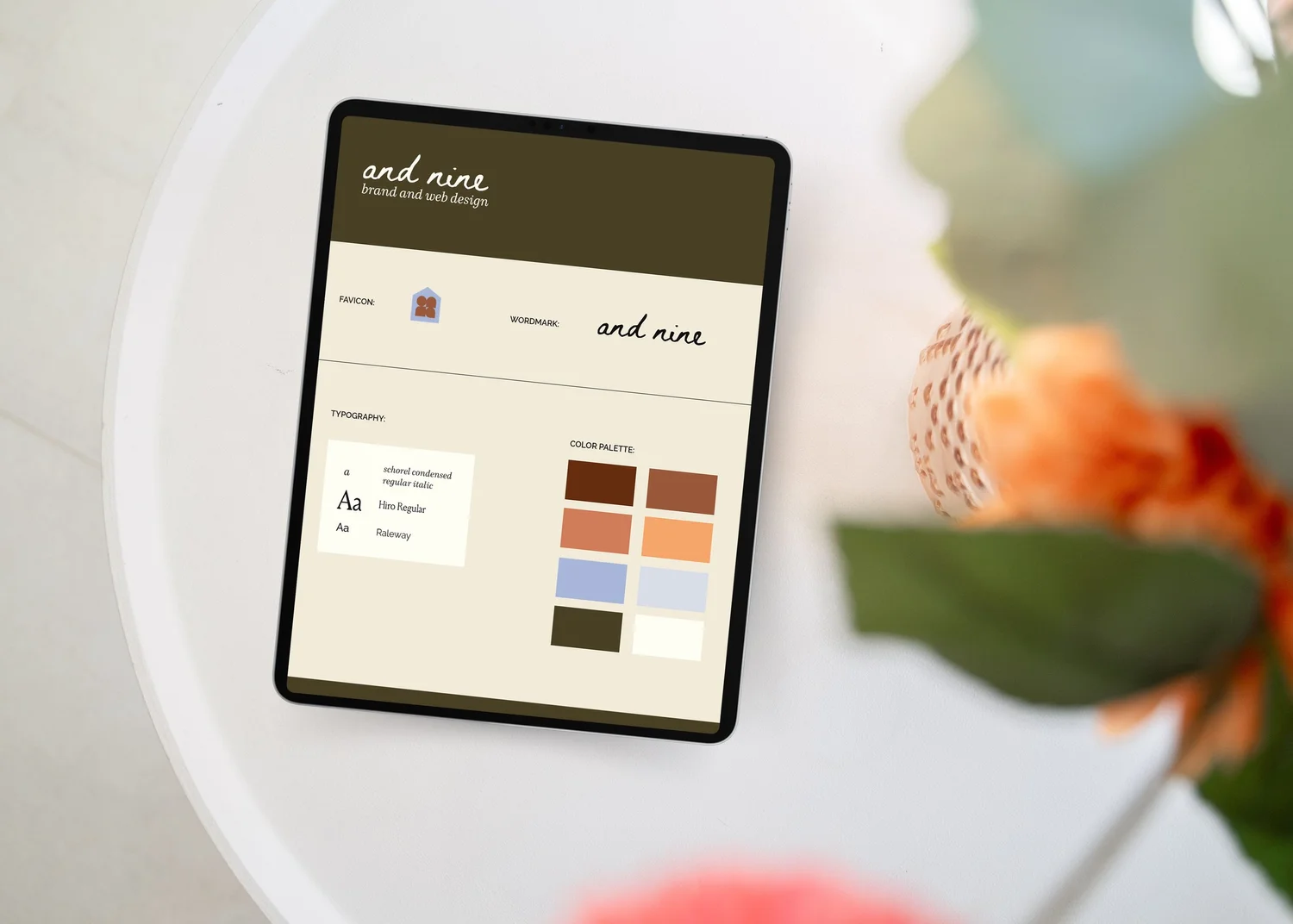 an Ipad resting on a table of orange flowers and the screen shows the brand identity for And Nine Design